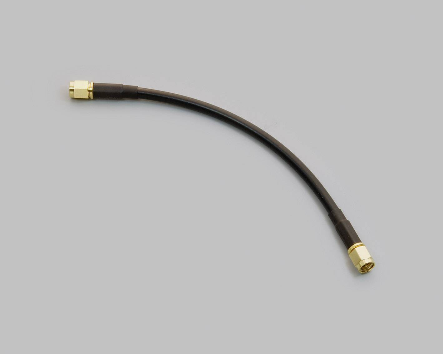 Koaxiální kabel se zlatými konektory na obou koncích na šedém pozadí.
