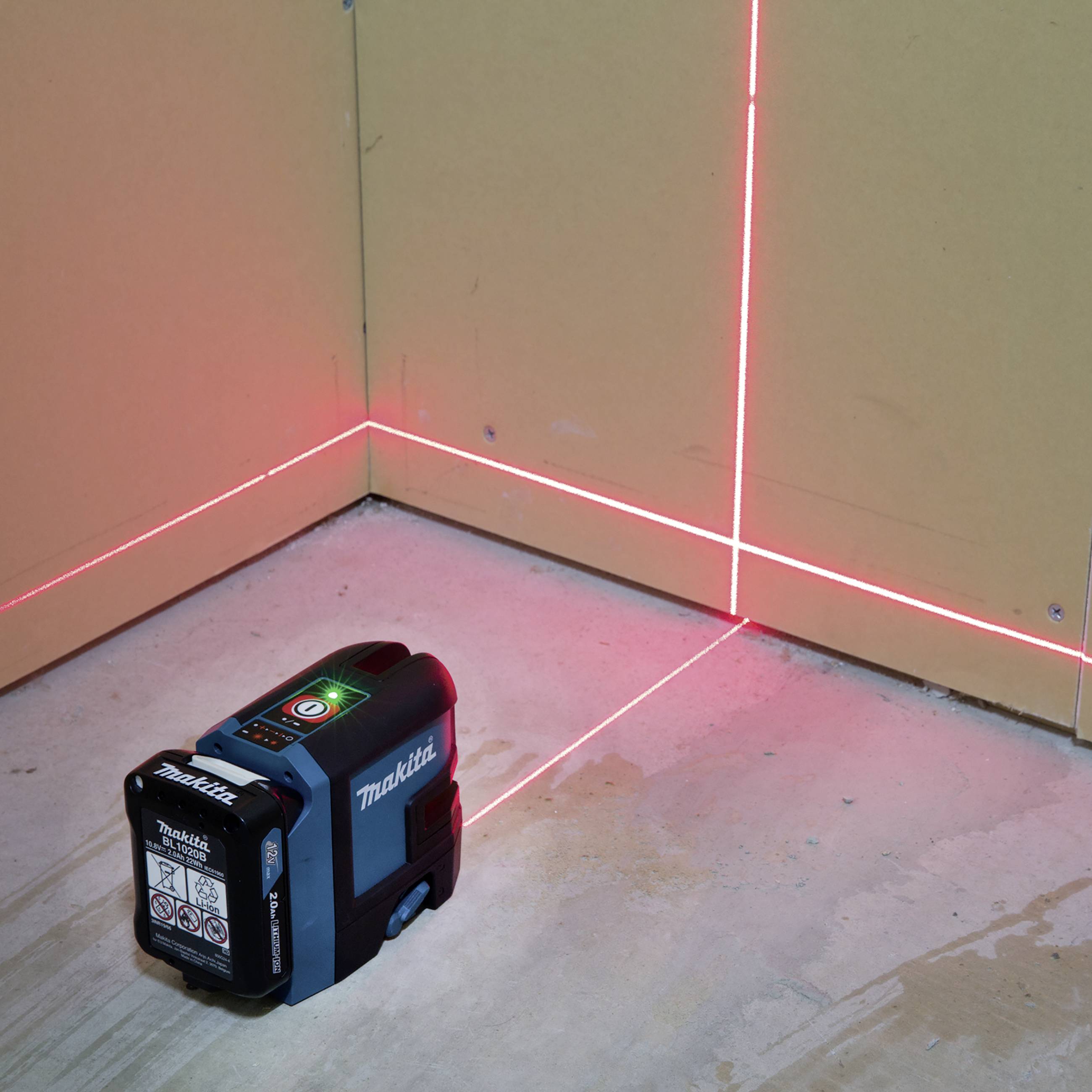 Zelený laserový nivelační přístroj promítá přesné červené linie na stěny a podlahu v místnosti, aby usnadnil vyrovnávání.