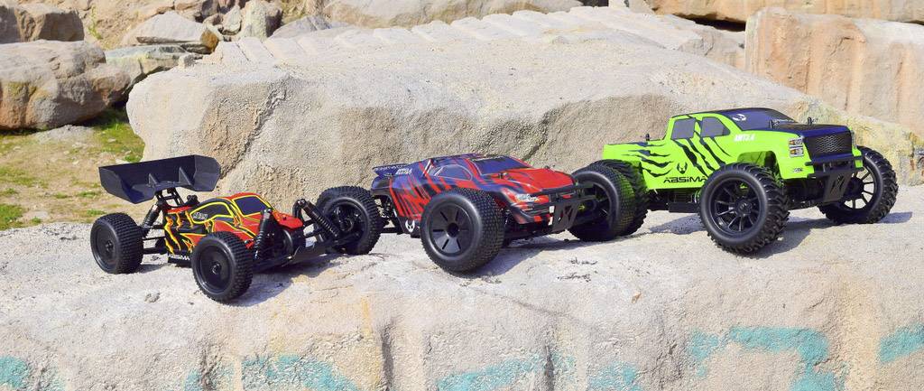 Tři dálkově ovládané vozy na velkých skalách. Vlevo: Buggy model v červeno-černé barvě. Uprostřed: Auto v červeno-černé barvě. Vpravo: Zelený truck.