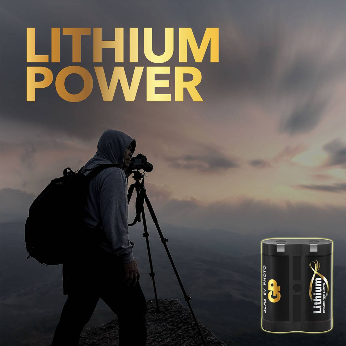 Muž s fotoaparátem na horském vrcholu při západu slunce, vedle lithiová baterie. Text: 'Lithium Power'. Symbolizuje energii a dobrodružství.