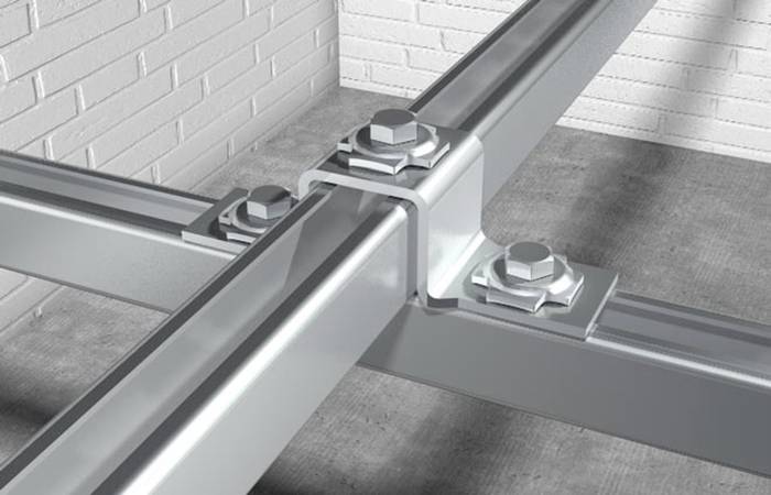 Kovový rám se šroubovanými spoji, upevněný na cihlové zdi na betonovém podkladu. Ukazuje konstrukční stabilitu a průmyslový způsob výstavby.