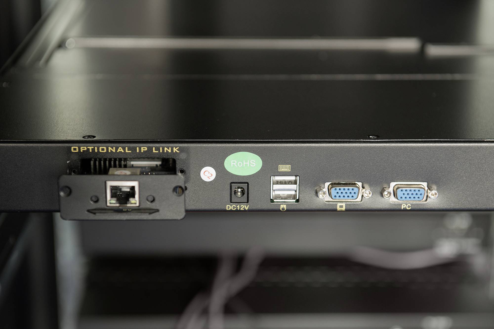Černé zařízení s několika porty: síťový kabel, USB, VGA a DC12V. Je viditelná zelená nálepka RoHS.