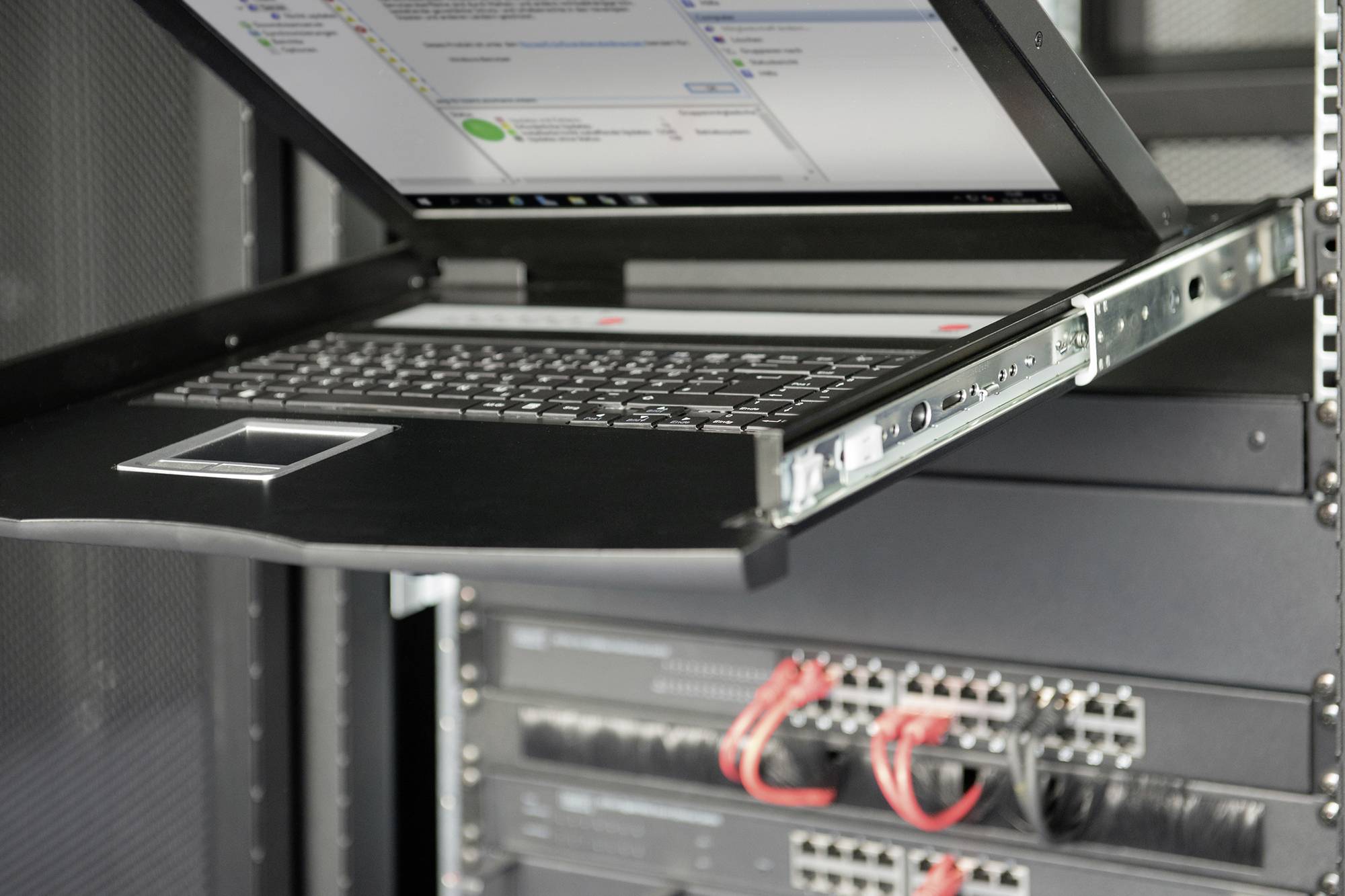 KVM přepínač s klávesnicí a monitorem je integrován do serverové skříně. Pod ním jsou viditelná síťová zařízení s připojenými kabely.
