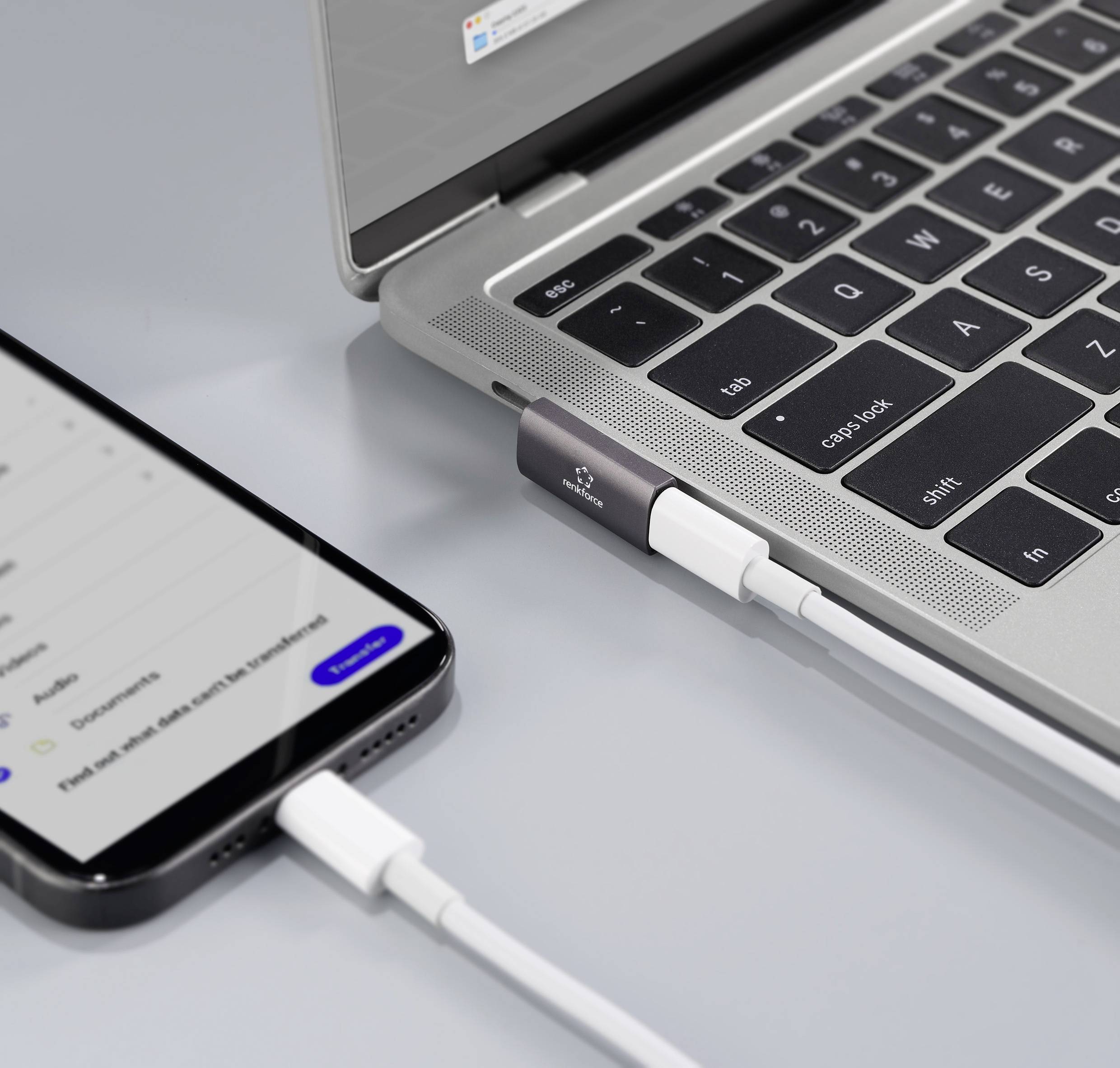 Mobilní telefon je připojen kabelem k laptopu, který leží na stole. Obrazovka laptopu zobrazuje nabíjecí obrazovku.