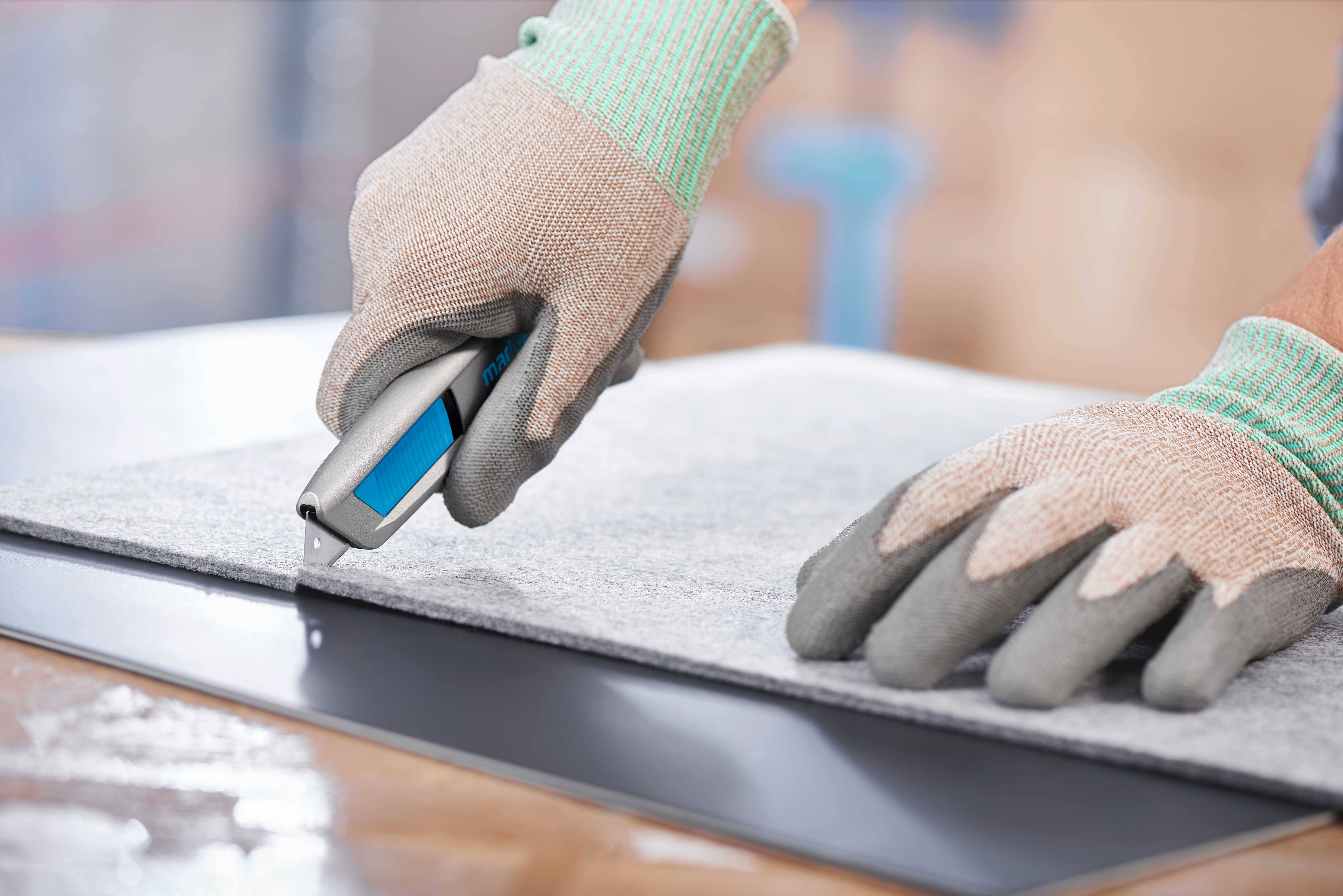 Osoba v rukavicích řeže řezacím nožem šedý materiál na rovném povrchu.