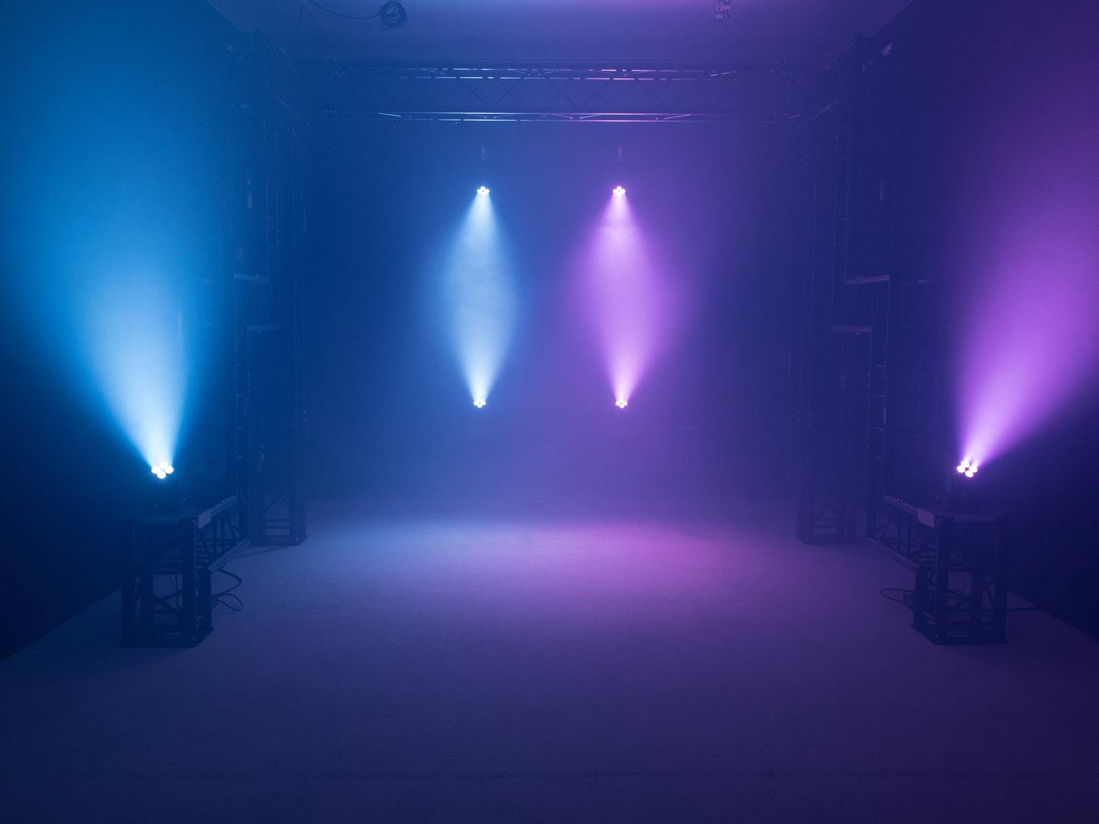 Tři reflektory vyzařují modré a fialové světlo v tmavé místnosti a vytvářejí atmosférickou náladu.