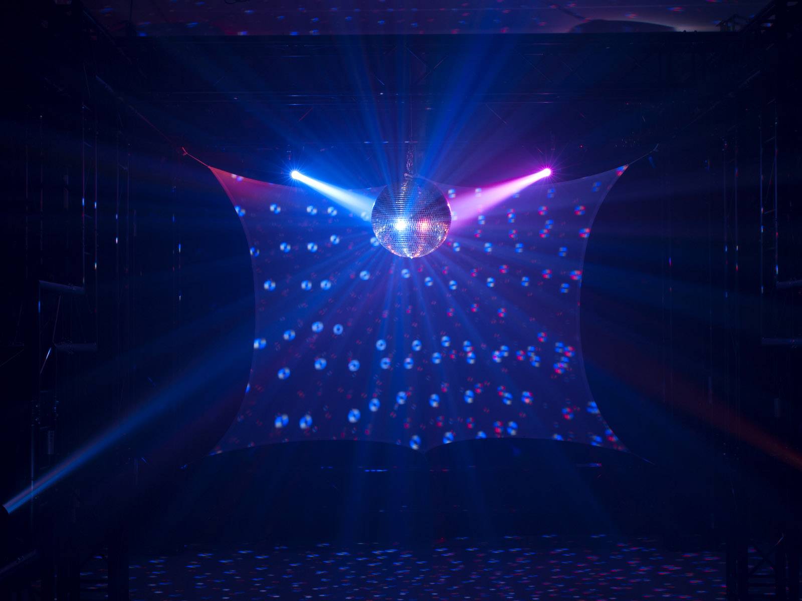 Disco koule visí na stropě tmavé místnosti, barevná světla a vzory vyzařují různými směry.