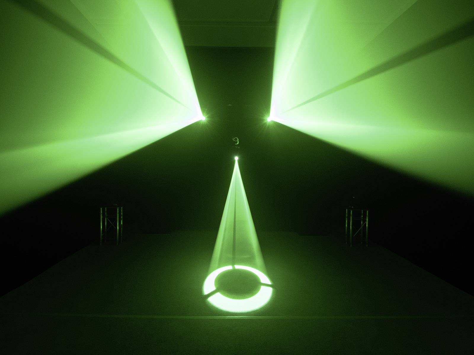 Zelené laserové světlo vyzařuje z několika zdrojů v temné místnosti, protíná se a vytváří geometrické vzory na podlaze.