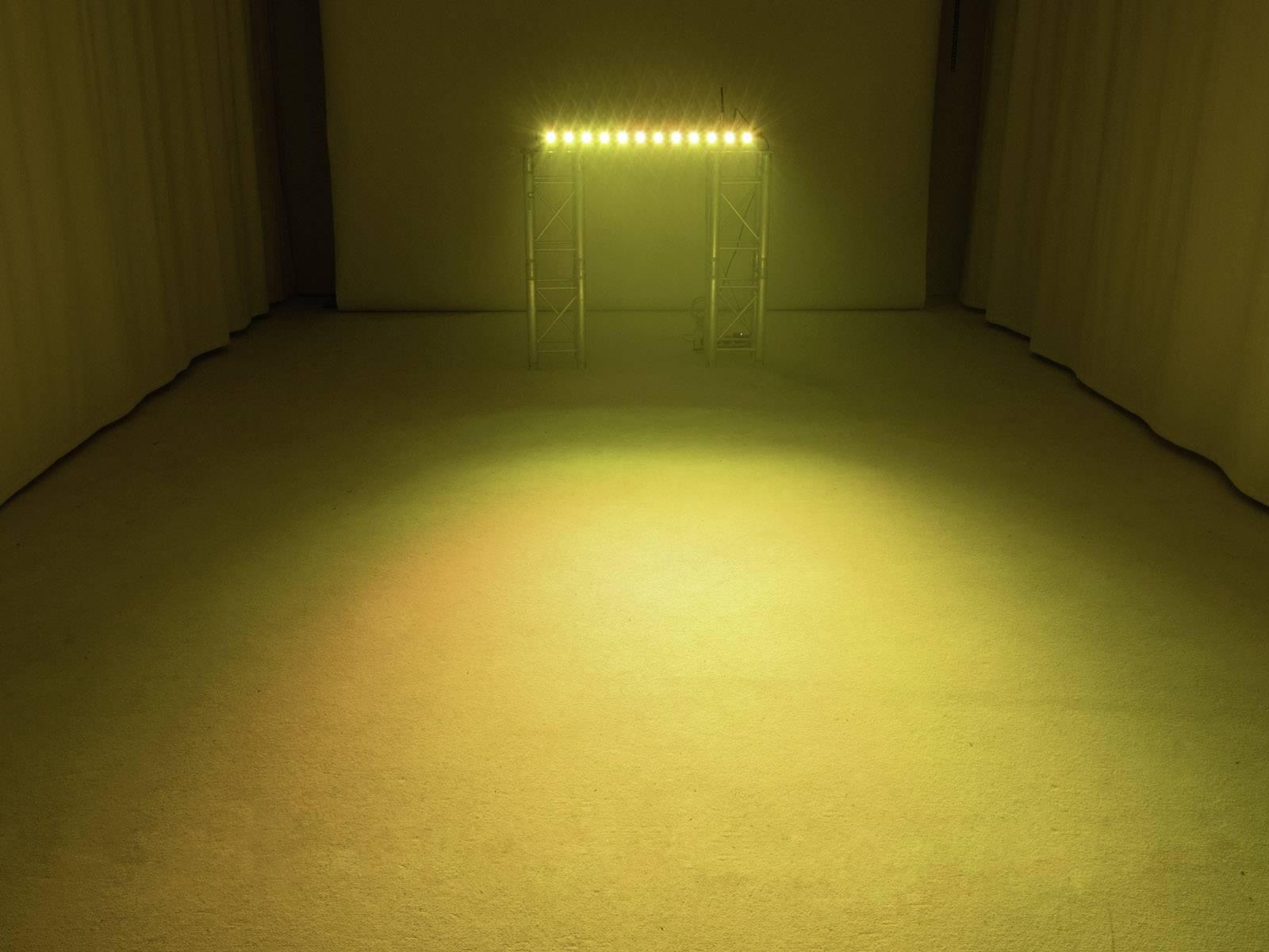 Prostý prostor s teplým žlutým světlem vyzařujícím z malého pódia osvětleného reflektory, minimalistické prostředí.