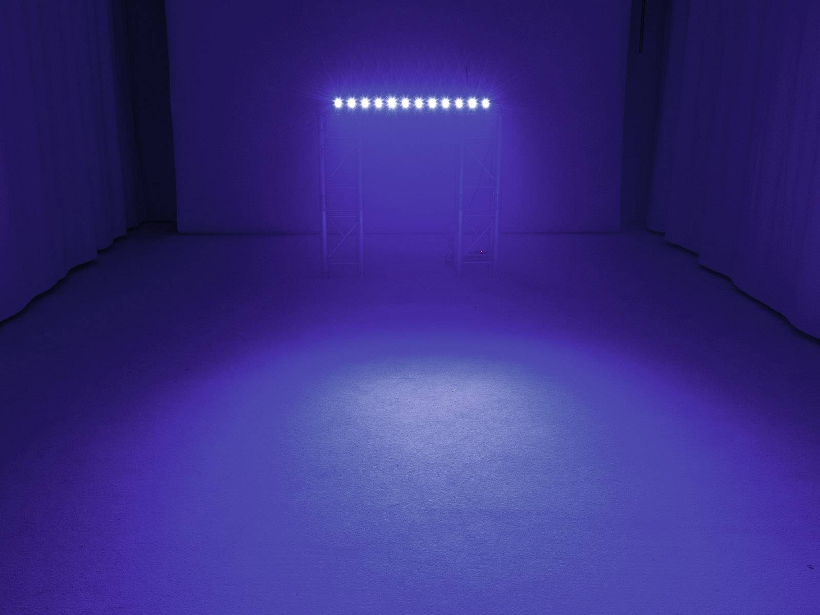 Modrý LED reflektor osvětluje podlahu v tmavé místnosti. Světlo vytváří zářící kruh na podlaze.