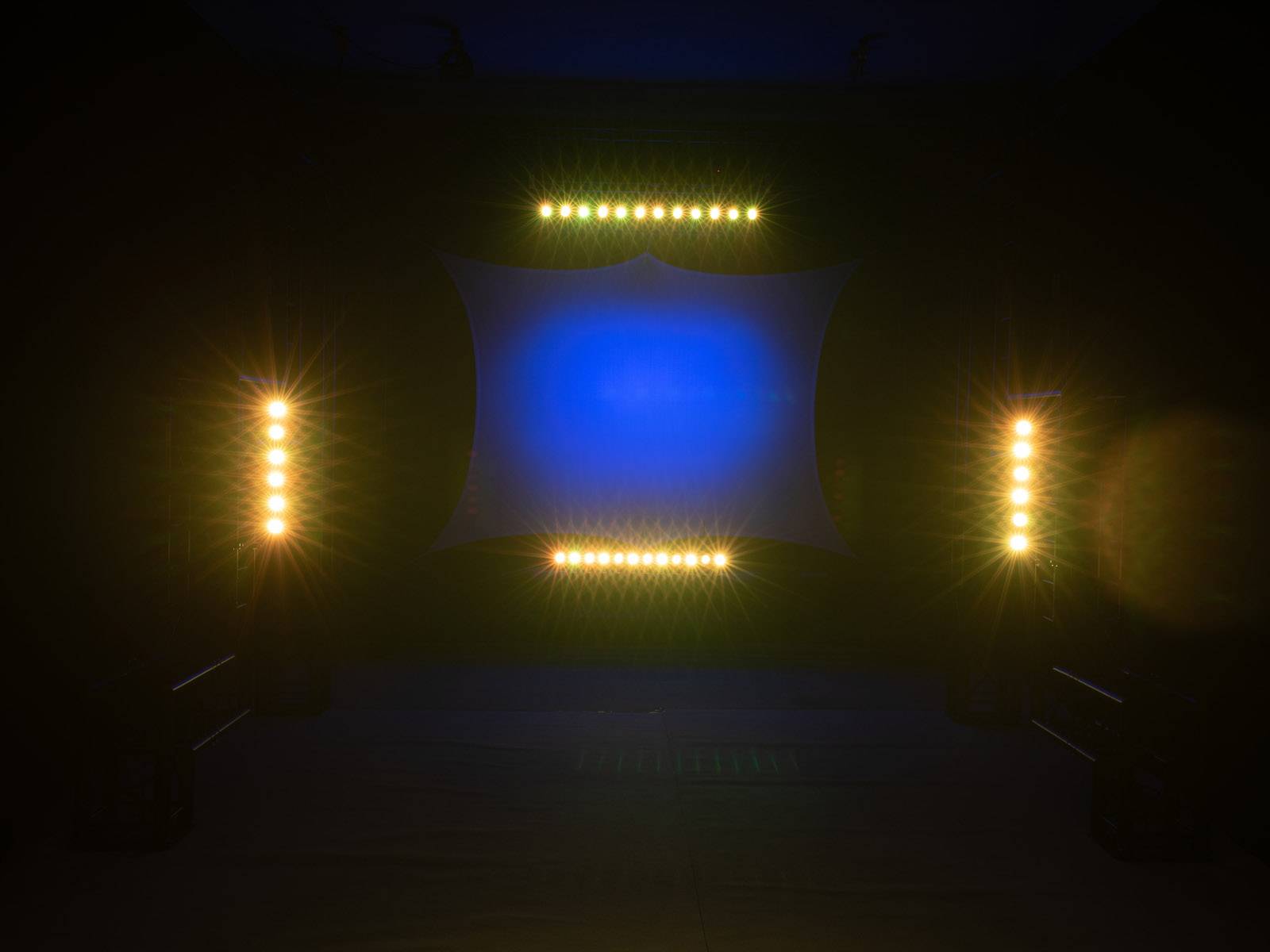 Jeviště s barevnými světly; modré světlo v pozadí, obklopené teplými bílými reflektory, vytváří dramatickou atmosféru.
