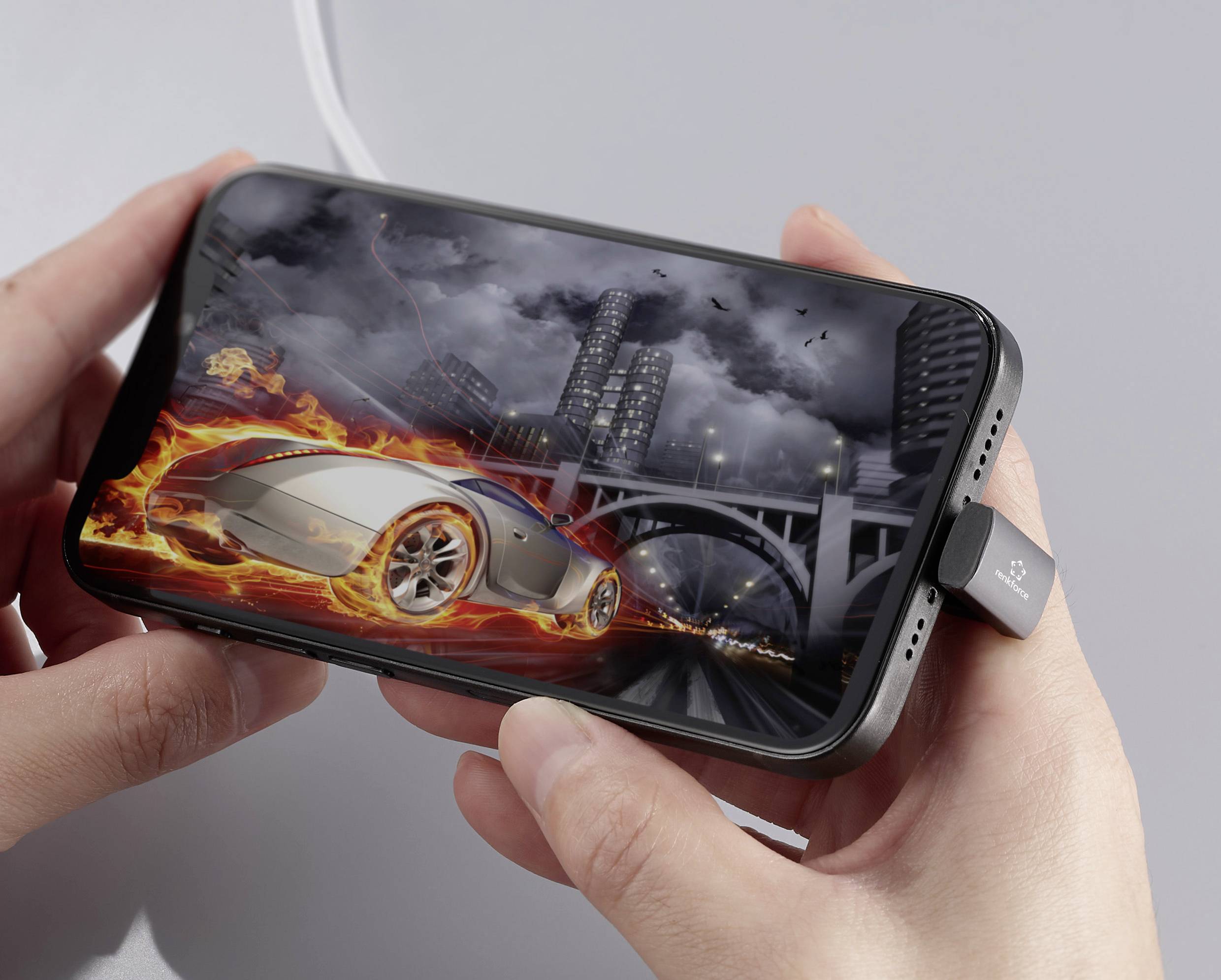 Osoba drží smartphone, na kterém je zobrazena závodní hra, kde futuristické auto projíždí osvětleným městem.
