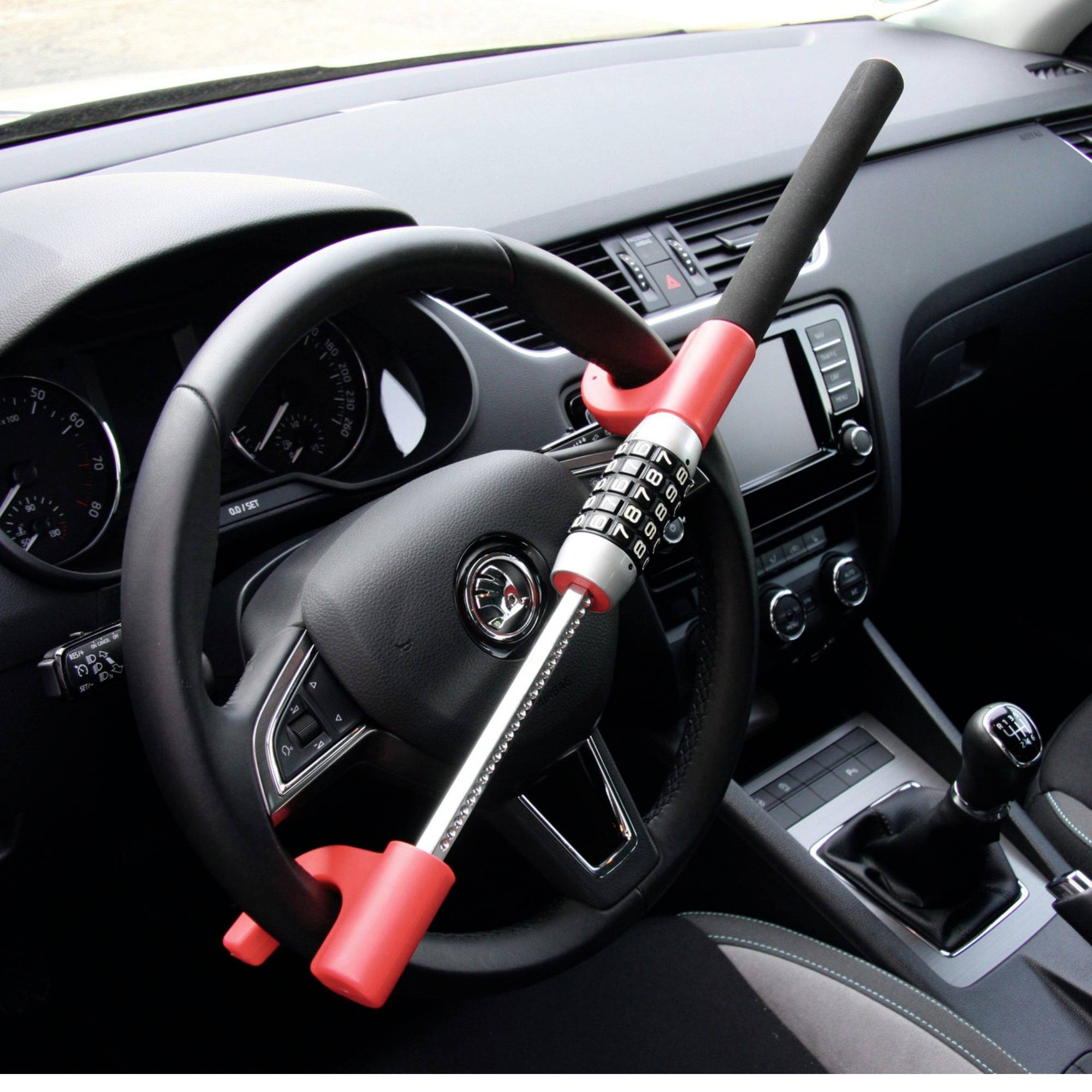 Vnitřek automobilu s volantem, na němž je připevněno zabezpečovací zařízení s číselným zámkem proti krádeži.