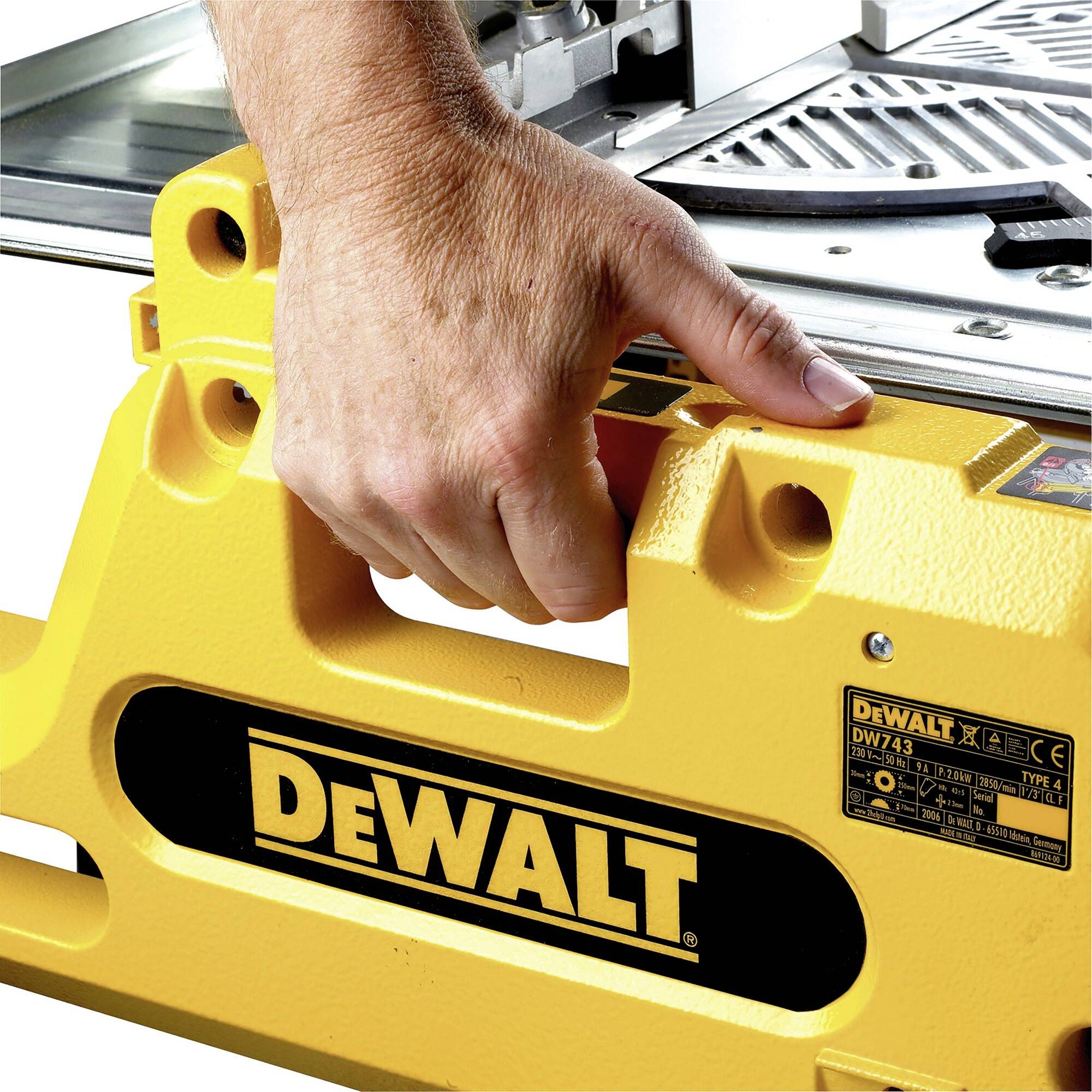 Jedna ruka obsluhuje žlutou pilu DeWalt, která je upevněná na pracovním stole. Logo DeWalt je na stroji zřetelně viditelné.