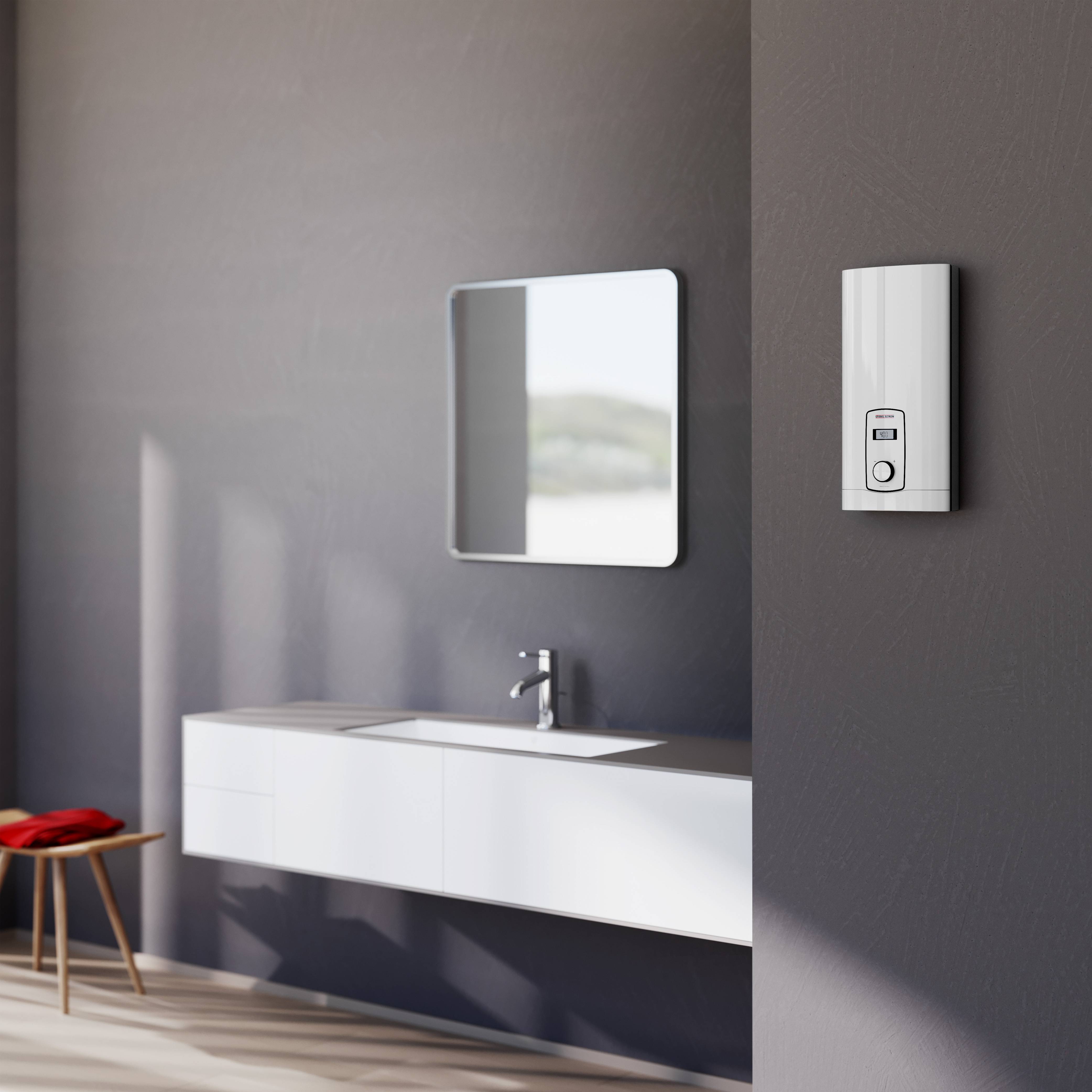 Moderní koupelna se zrcadlem, nástěnným umyvadlem a moderním ohřívačem vody na šedé stěně. Vedle stojí červená stolička.