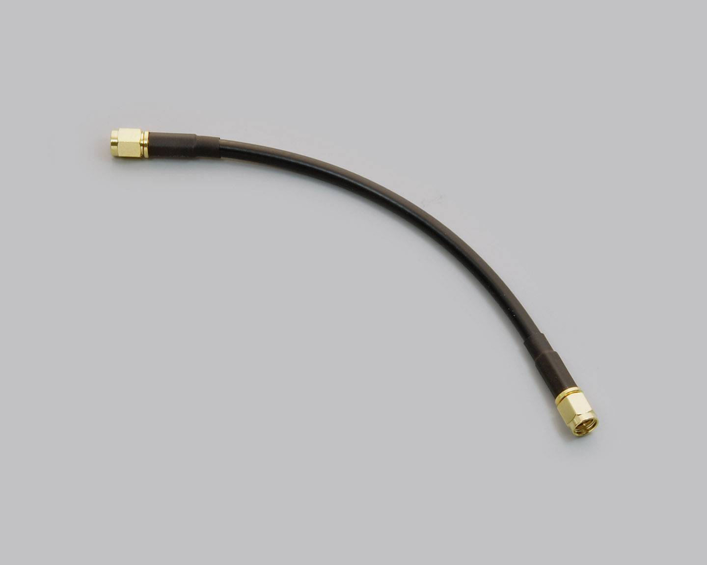 Krátký černý koaxiální kabel se zlatými konektory na obou koncích na šedém pozadí.