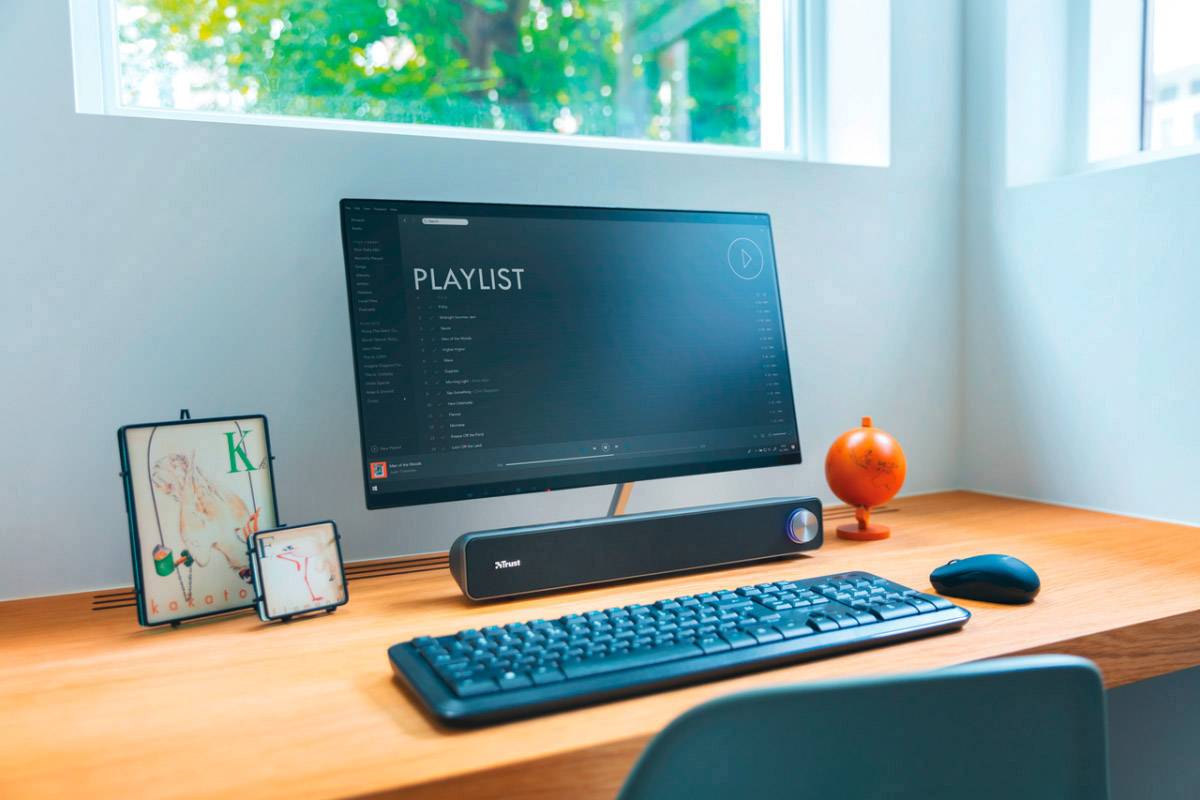 Počítačové pracoviště s obrazovkou zobrazující 'playlist', klávesnicí, myší a dekorativními prvky na stole.