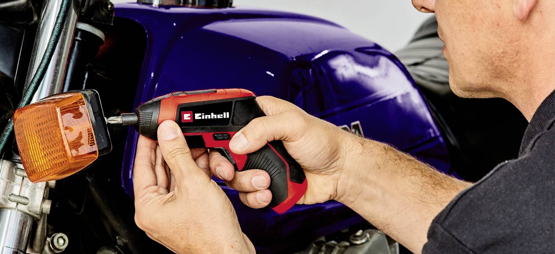 Osoba opravuje motocykl a používá bezdrátový šroubovák k utažení blinkru.