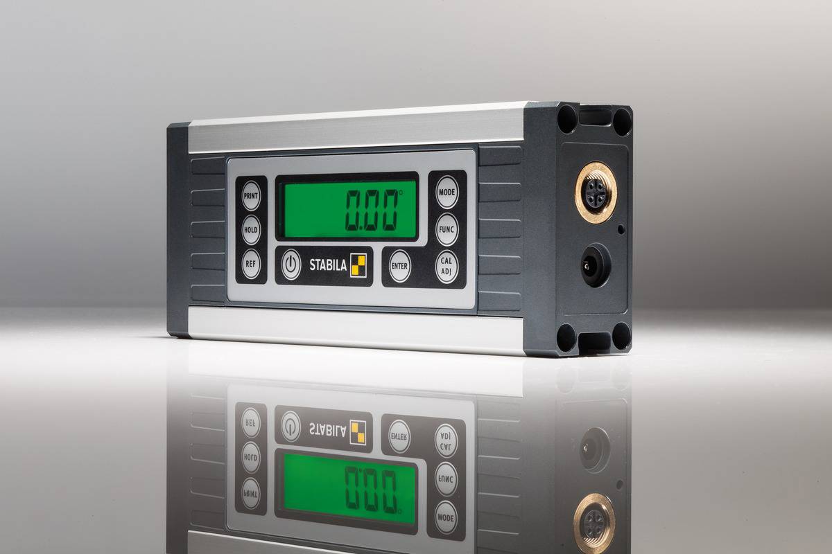 Digitální úhloměr se zeleným displejem, zobrazující '0.00'. Obklopen šedým a černým pouzdrem, umístěn na reflexním povrchu.