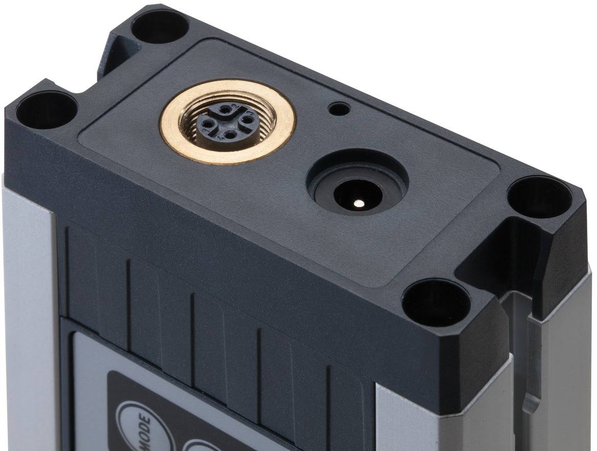 Obdélníkový technický konektor s kulatým připojením uprostřed a menším otvorem vedle něj.