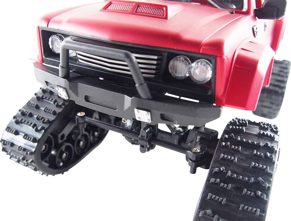 Červené hračkové auto s pásy místo kol v popředí, na bílém pozadí, vykazuje robustní design.