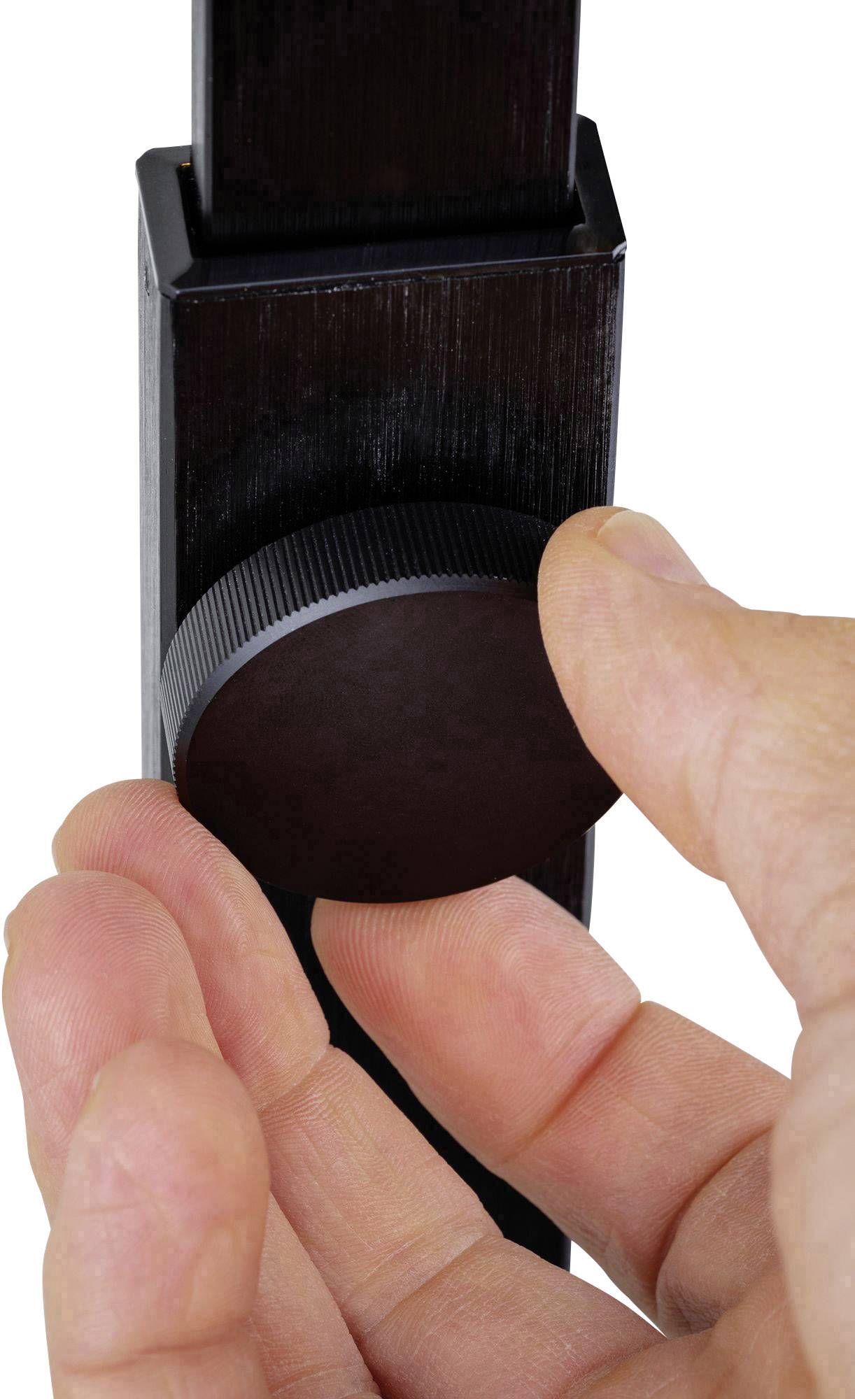 Jedna ruka otáčí kulatým vroubkovaným knoflíkem na černém kovovém stojanu.