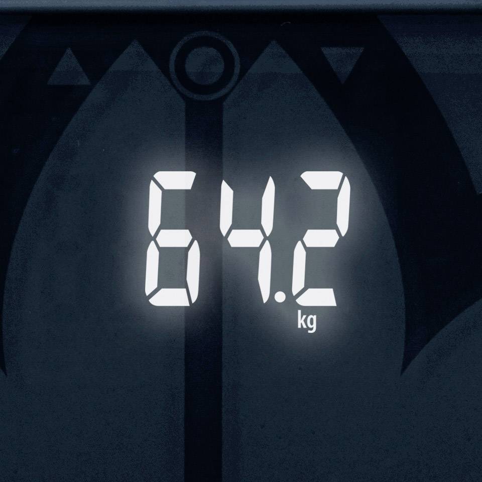 Digitální displej ukazuje 64,2 kg na tmavém pozadí.