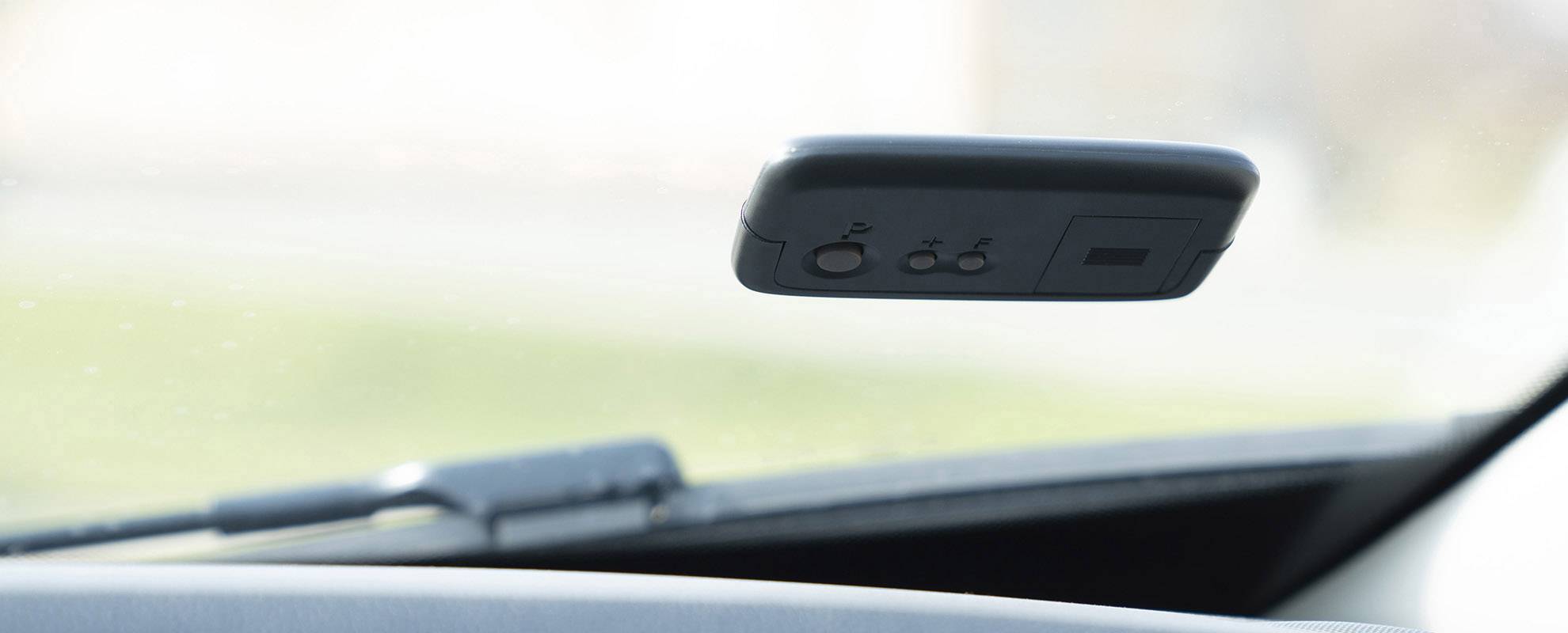 Zpětné zrcátko se třemi tlačítky pro ovládání; je připevněno na čelním skle automobilu.