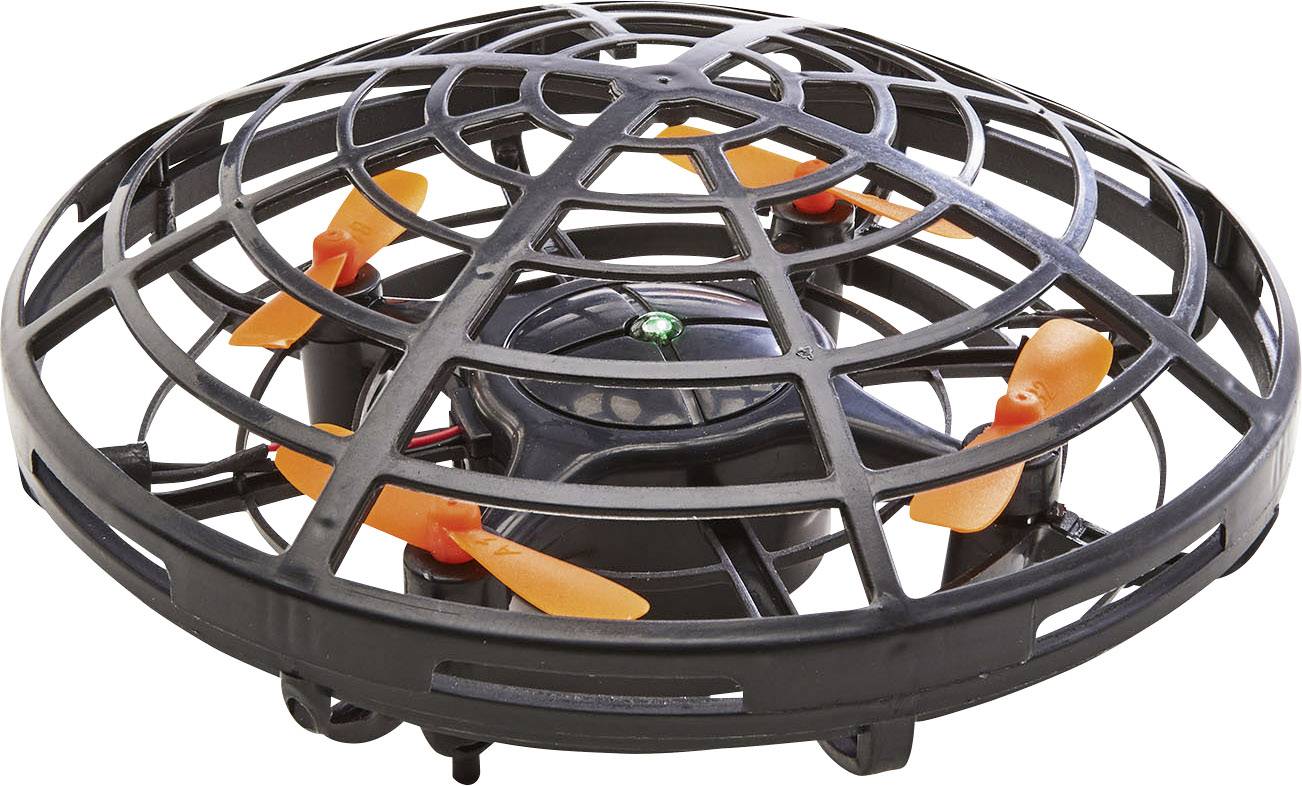 Černý dron s oranžovými vrtulemi, obklopený ochranným krytem, připravený k letu na bílém povrchu.