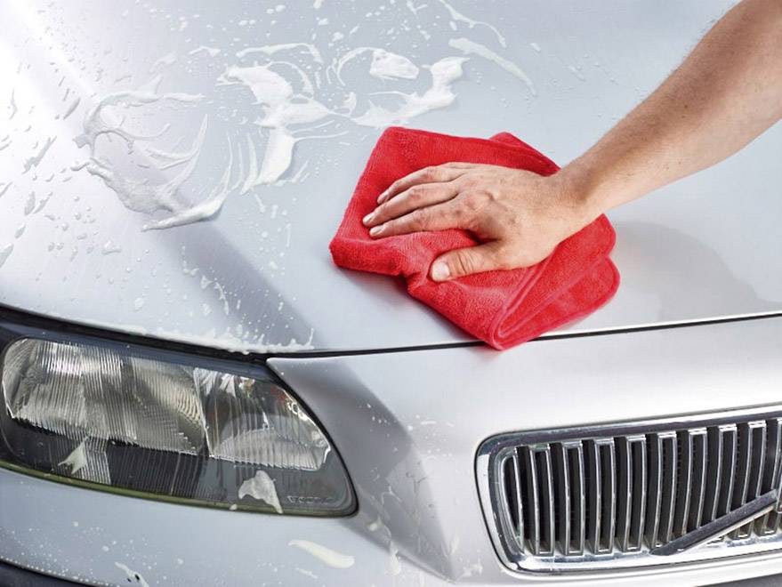 Ruka s červeným hadříkem leští kapotu stříbrného automobilu pokrytého mýdlovou vodou.