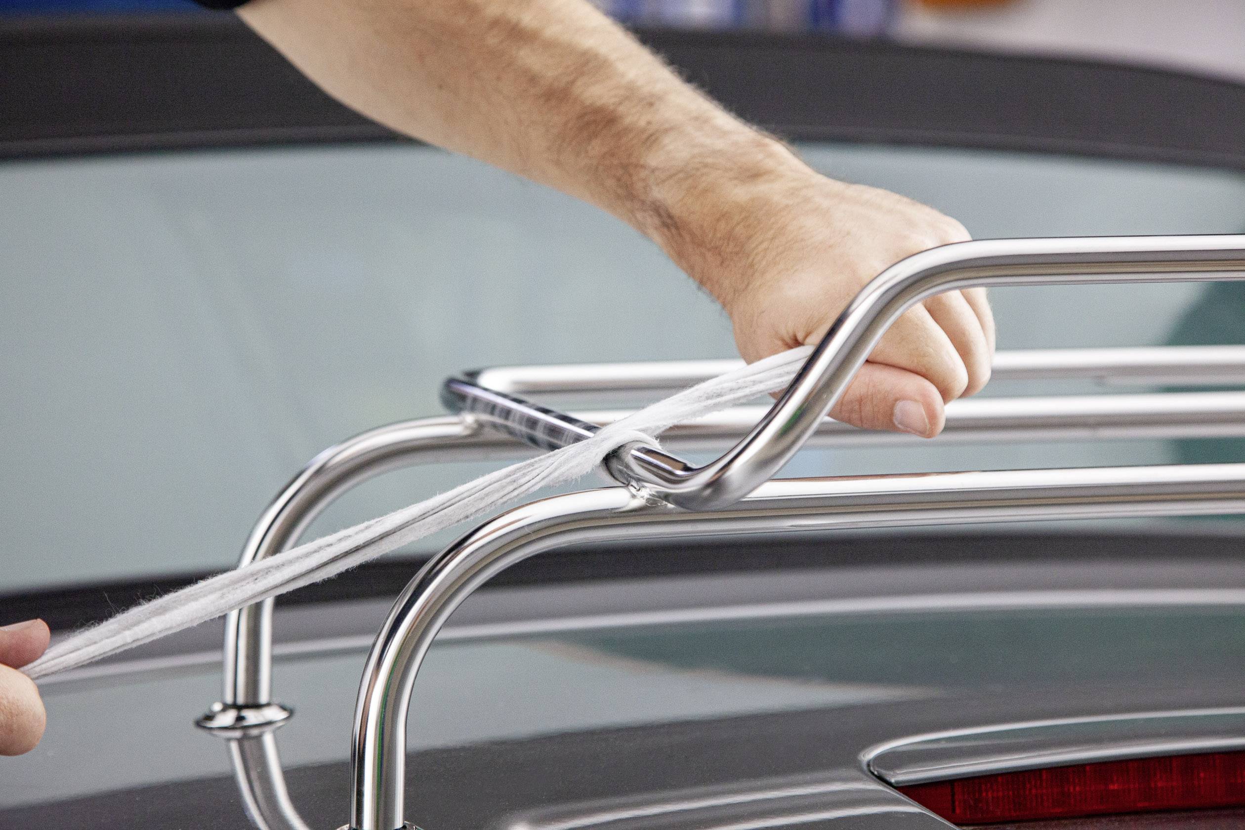 Jedna osoba upevňuje lano na stříbrném střešním nosiči automobilu.