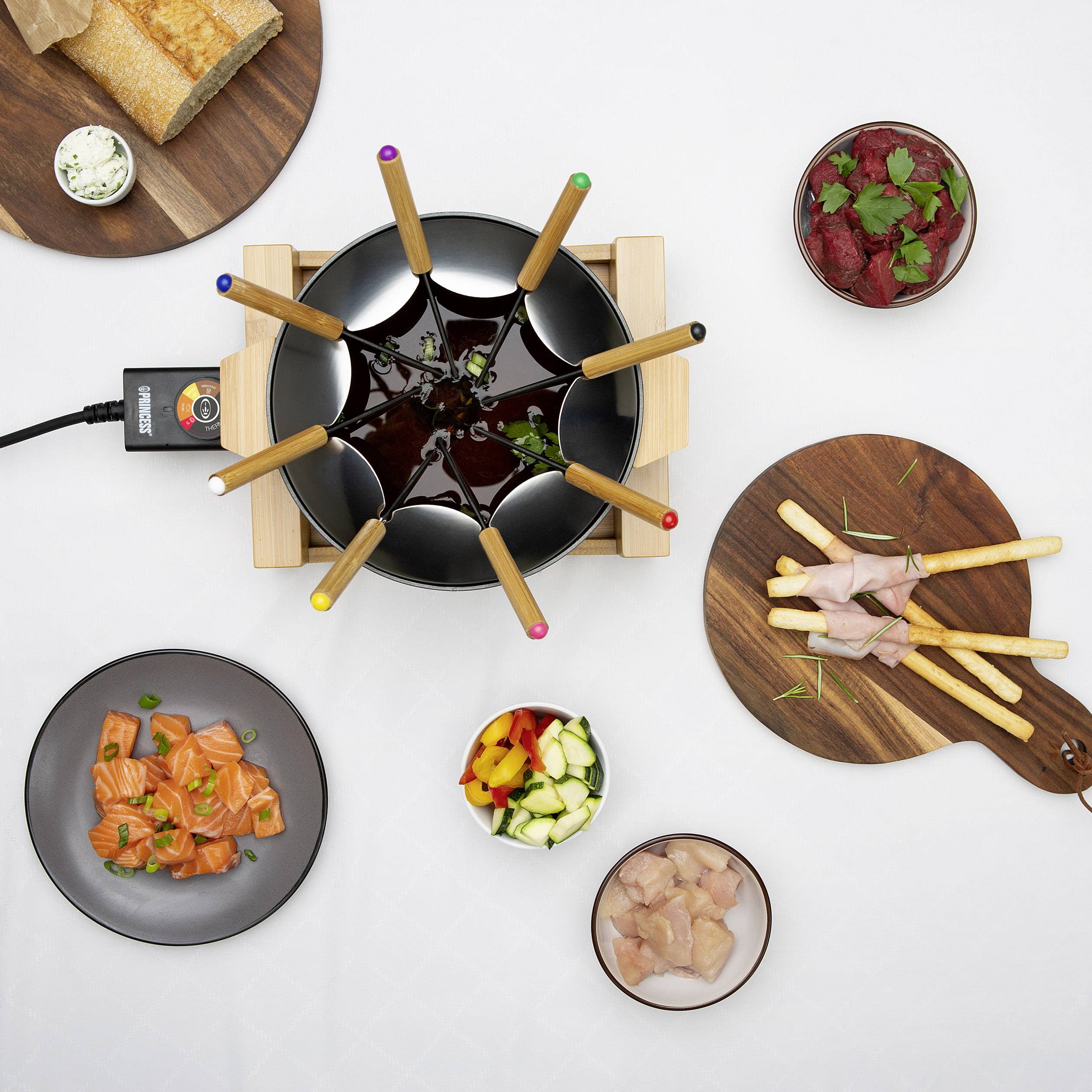 Fondue se zeleninou, masem, chlebem a omáčkami na stole. Šest vidliček je ponořeno ve fondue hrnci.
