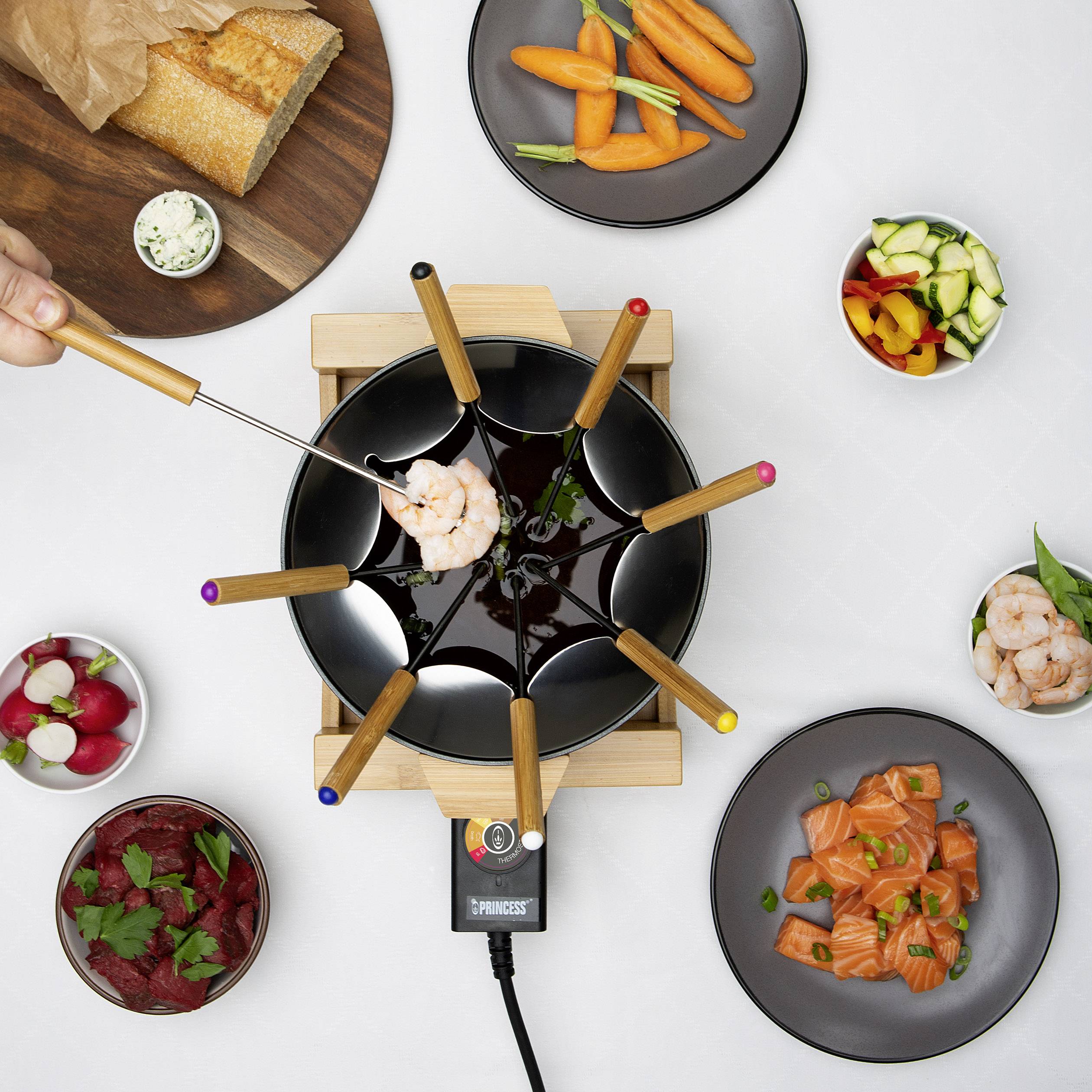Fondue set s různými ingrediencemi, jako jsou krevety, zelenina a chléb, umístěný na stole.