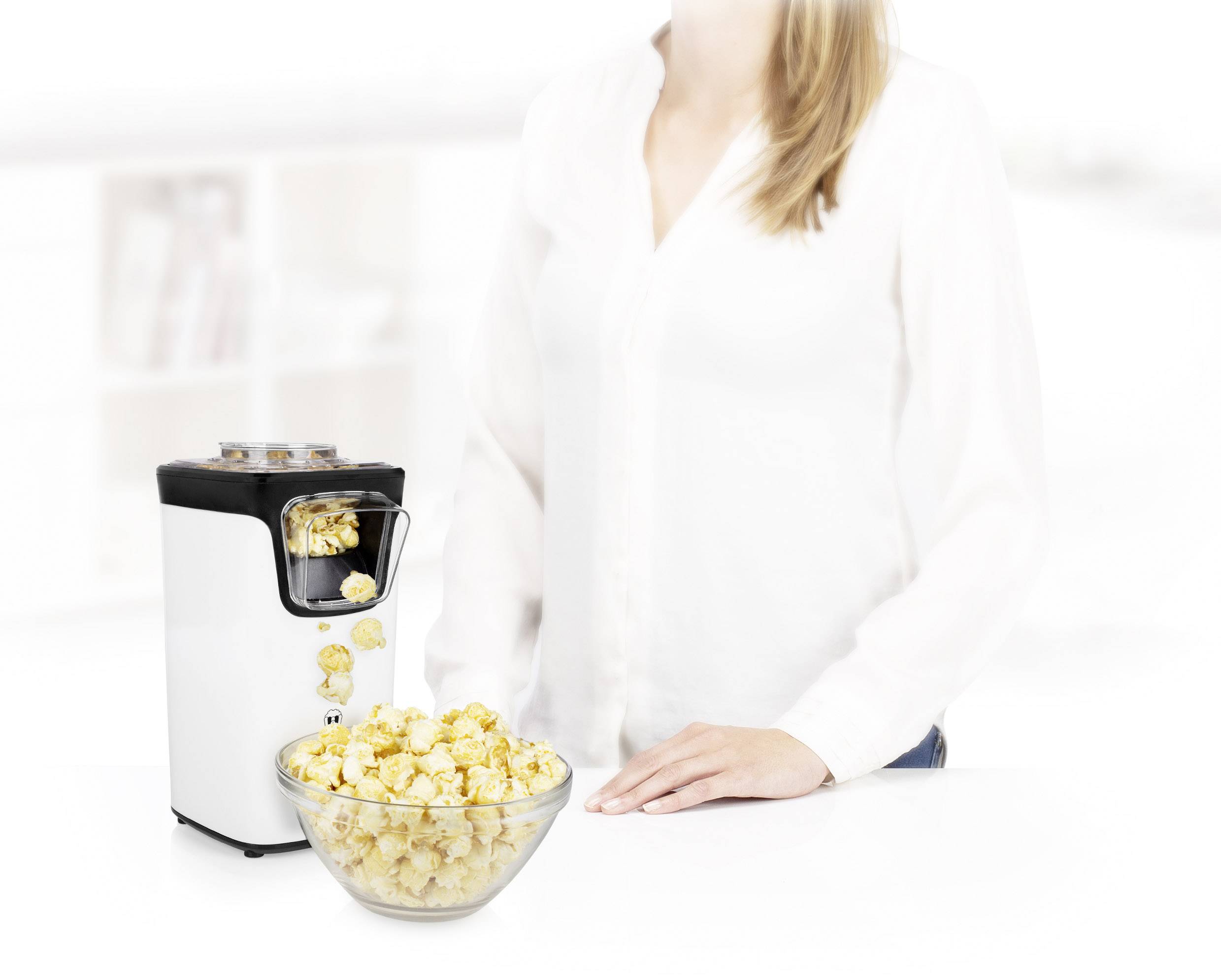 Vedle popcornovače stojícího na stole stojí jedna osoba. Před strojem je miska čerstvého popcornu.