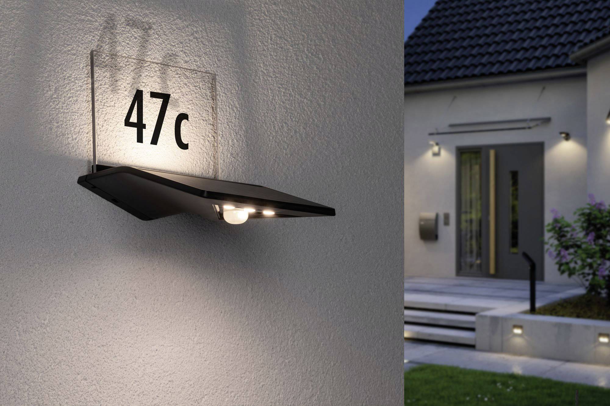 Pohled zvenčí na dům s moderním nástěnným osvětlením. Na čísle domu '47c' svítí elegantní lampa. Za soumraku.