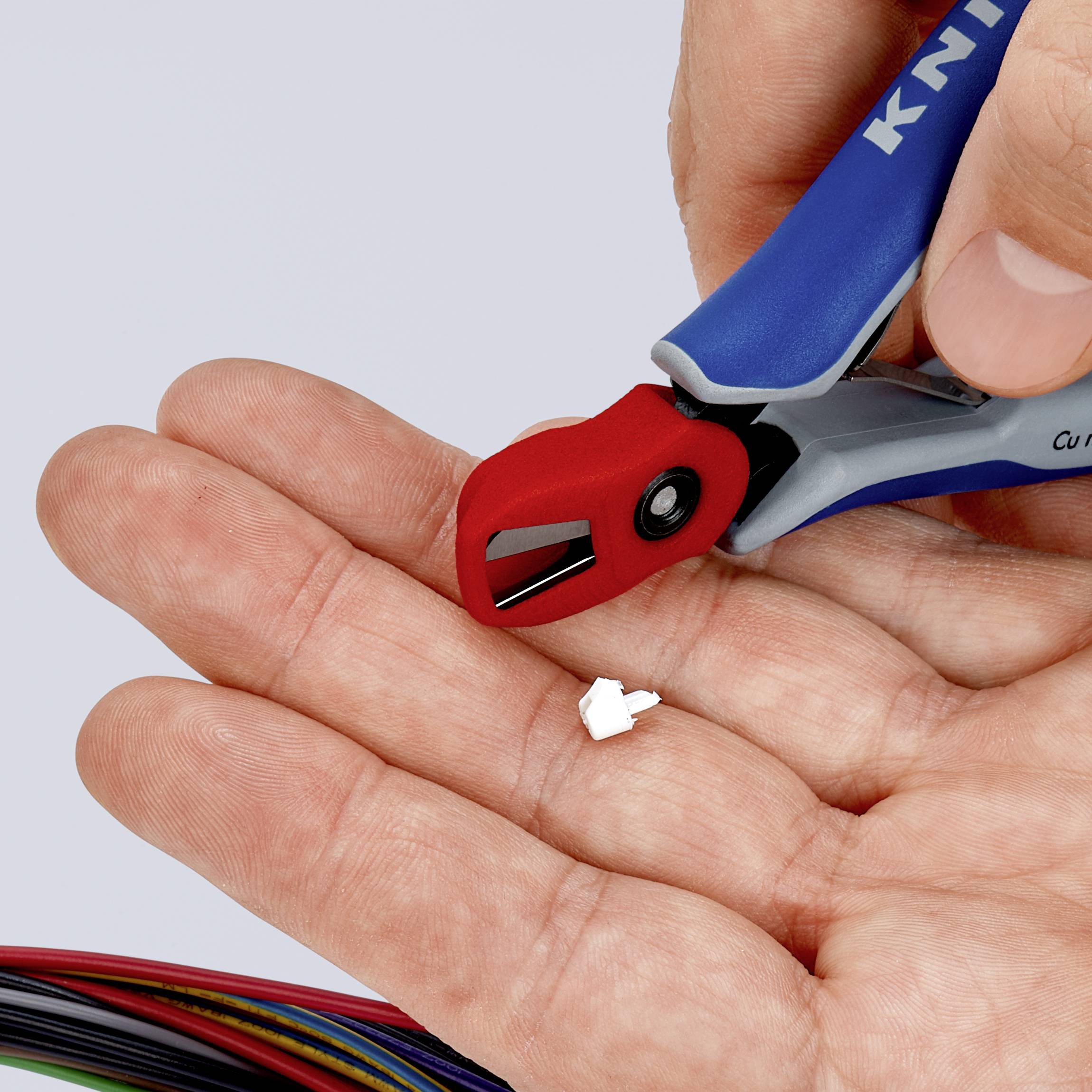 Jedna ruka drží malé červené štípací kleště, které odřezávají malý bílý konektor z konce vícebarevných kabelů.