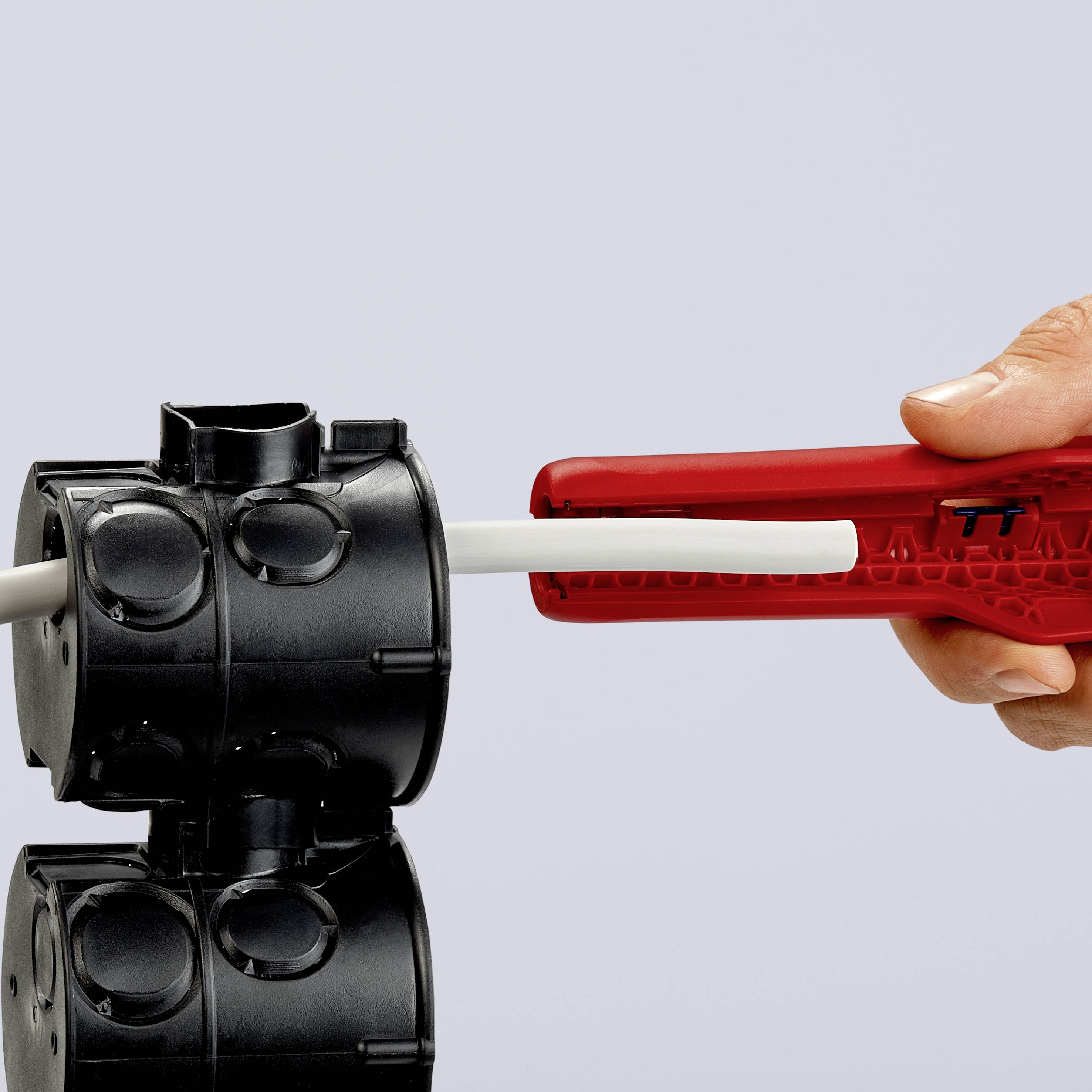Jedna ruka drží červenou trubku, která je zasazována do černého pouzdra, pravděpodobně během montážního procesu.