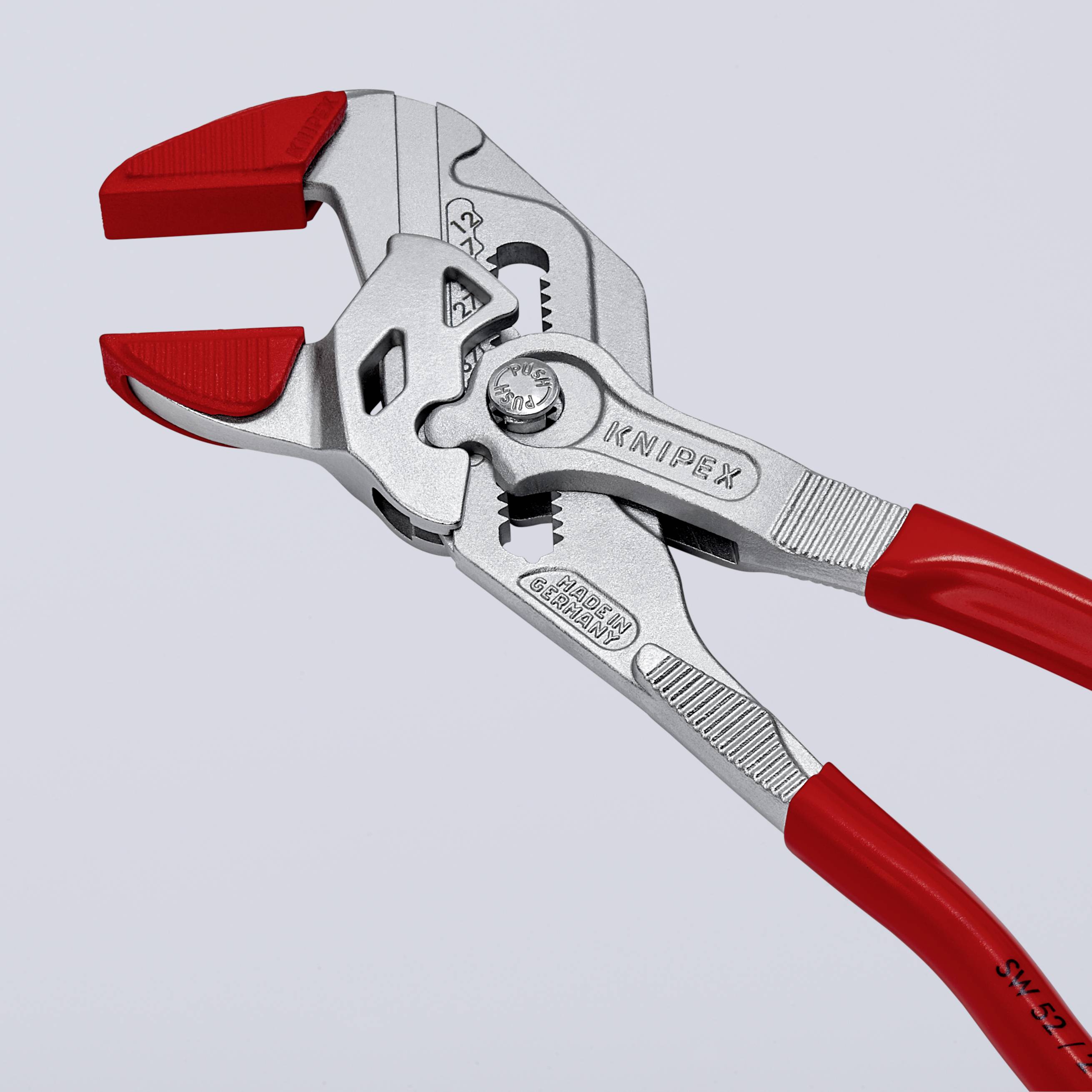 Stříbrné kleště s červenými rukojeťmi od značky 'Knipex' ležící, ukazující mechanismus otevírání a vtisknuté logo.