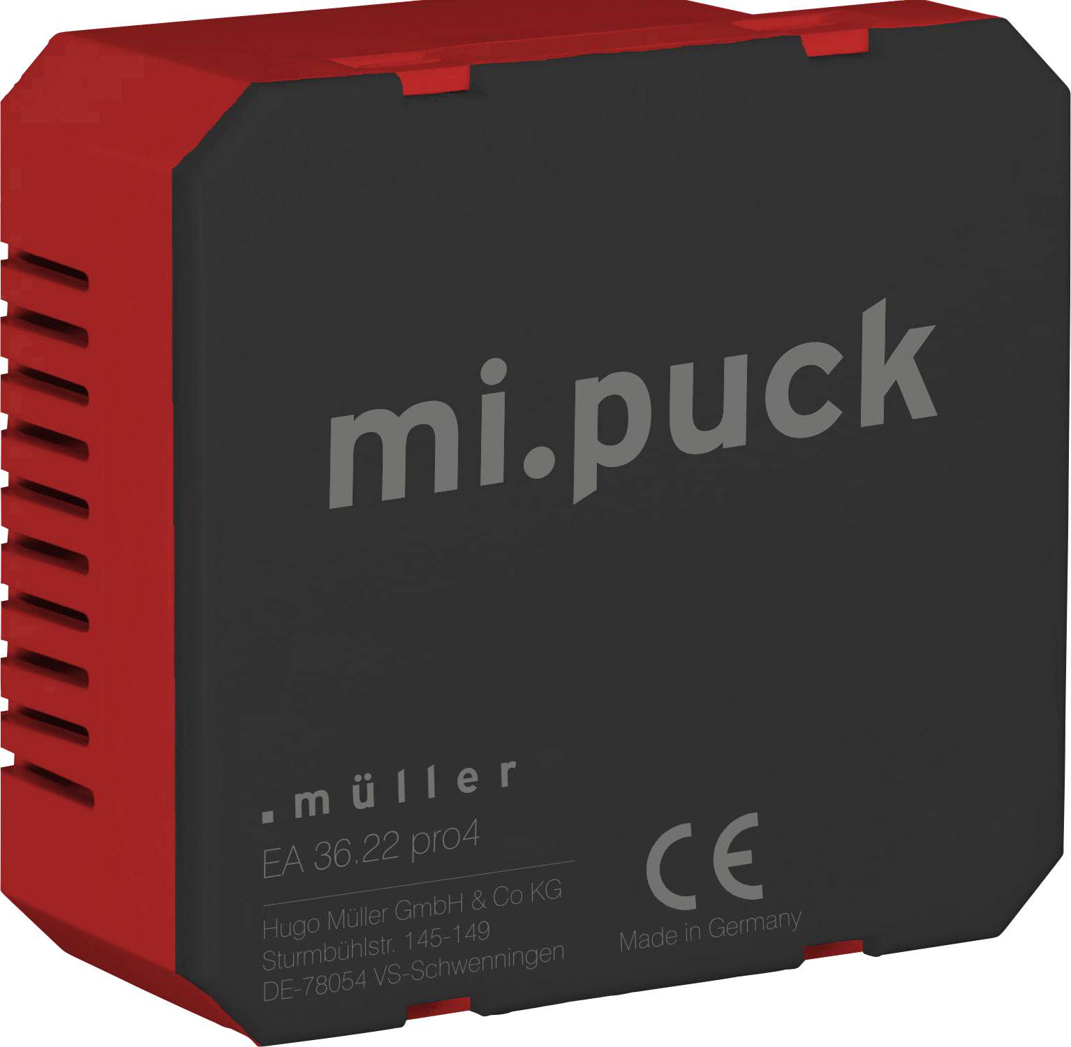 Červený, čtvercový technický adaptér s nápisem 'mi.puck' a označením CE. Vyroben společností Hugo Müller GmbH & Co KG v Německu.
