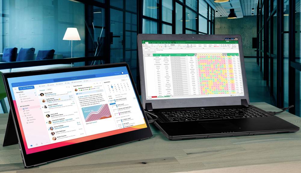Laptop a tablet leží na stole. Laptop zobrazuje barevnou tabulku, tablet ukazuje náhled e-mailu. V pozadí je kancelář.