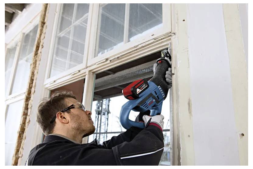 Osoba používá elektrické nářadí k demontáži okenního rámu, přičemž se soustředí na renovační práce uvnitř budovy.