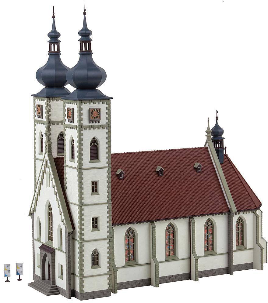 Kostel s červenými taštovými střechami a dvěma vysokými věžemi s cibulkovitými báněmi. Fasáda je bílá s dekorativními prvky.