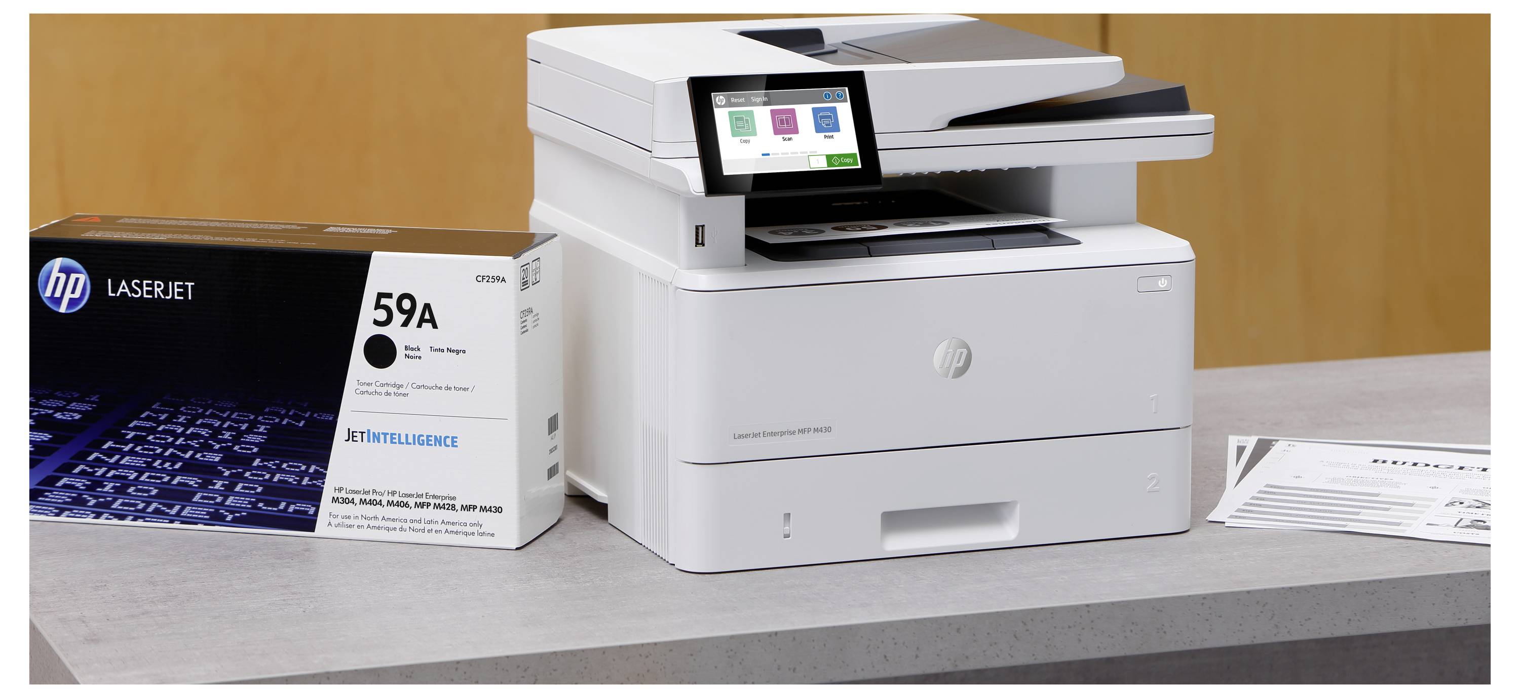 Tiskárna HP LaserJet na stole vedle krabice toneru '59A' a vytištěného listu, na kterém jsou vidět kancelářské tiskací zařízení.