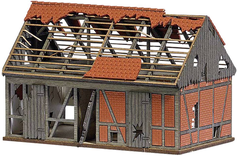 Miniaturní model zchátralého hrázděného domu s poškozenou střechou a děravými stěnami, který naznačuje rozpad nebo destrukci.
