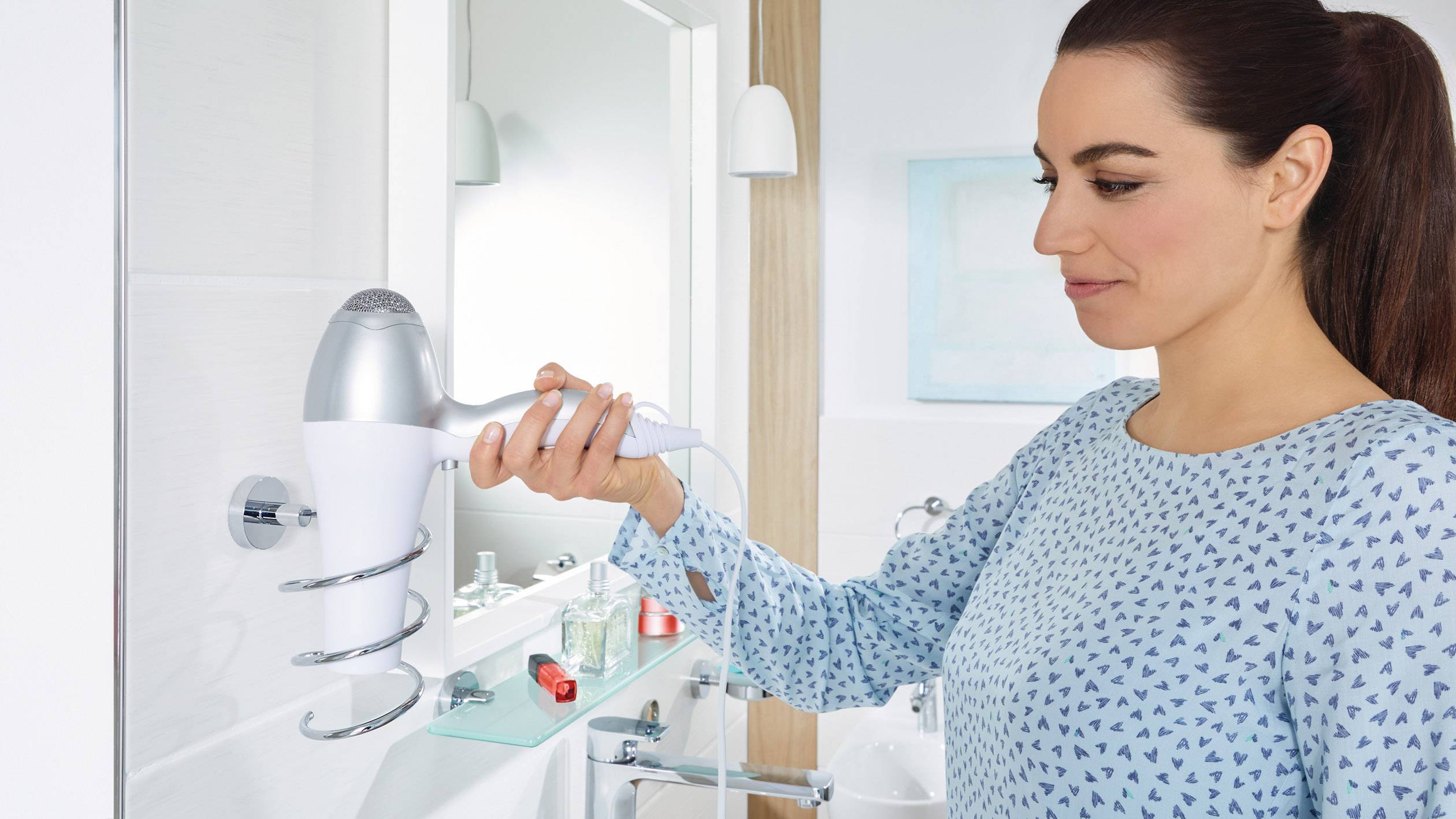 Žena používá bílý fén v koupelně s moderním designem. Stojí před zrcadlem a suší si vlasy.