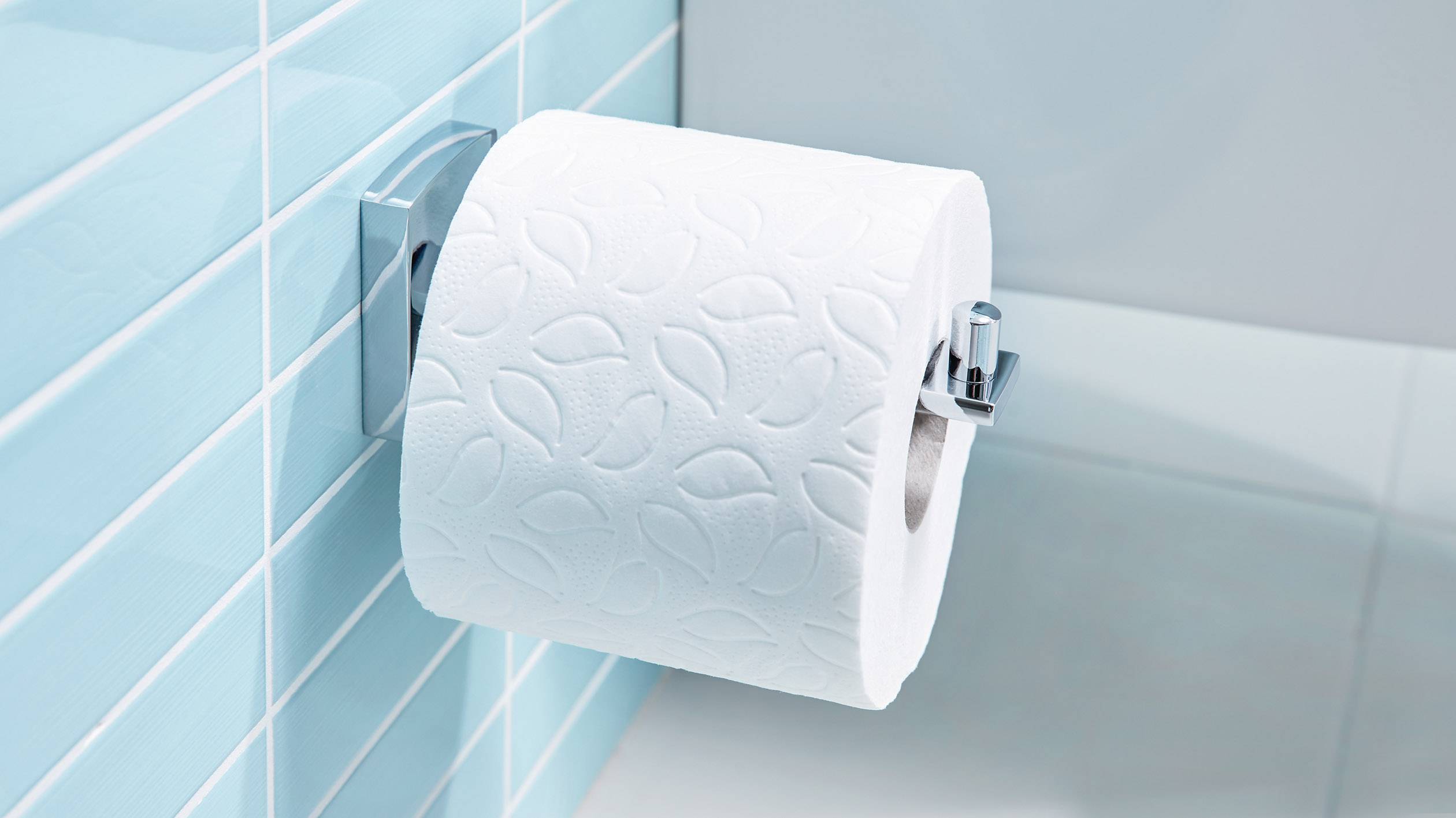 Toaletní papír na nerezovém držáku, připevněný na tyrkysové obložené stěně.