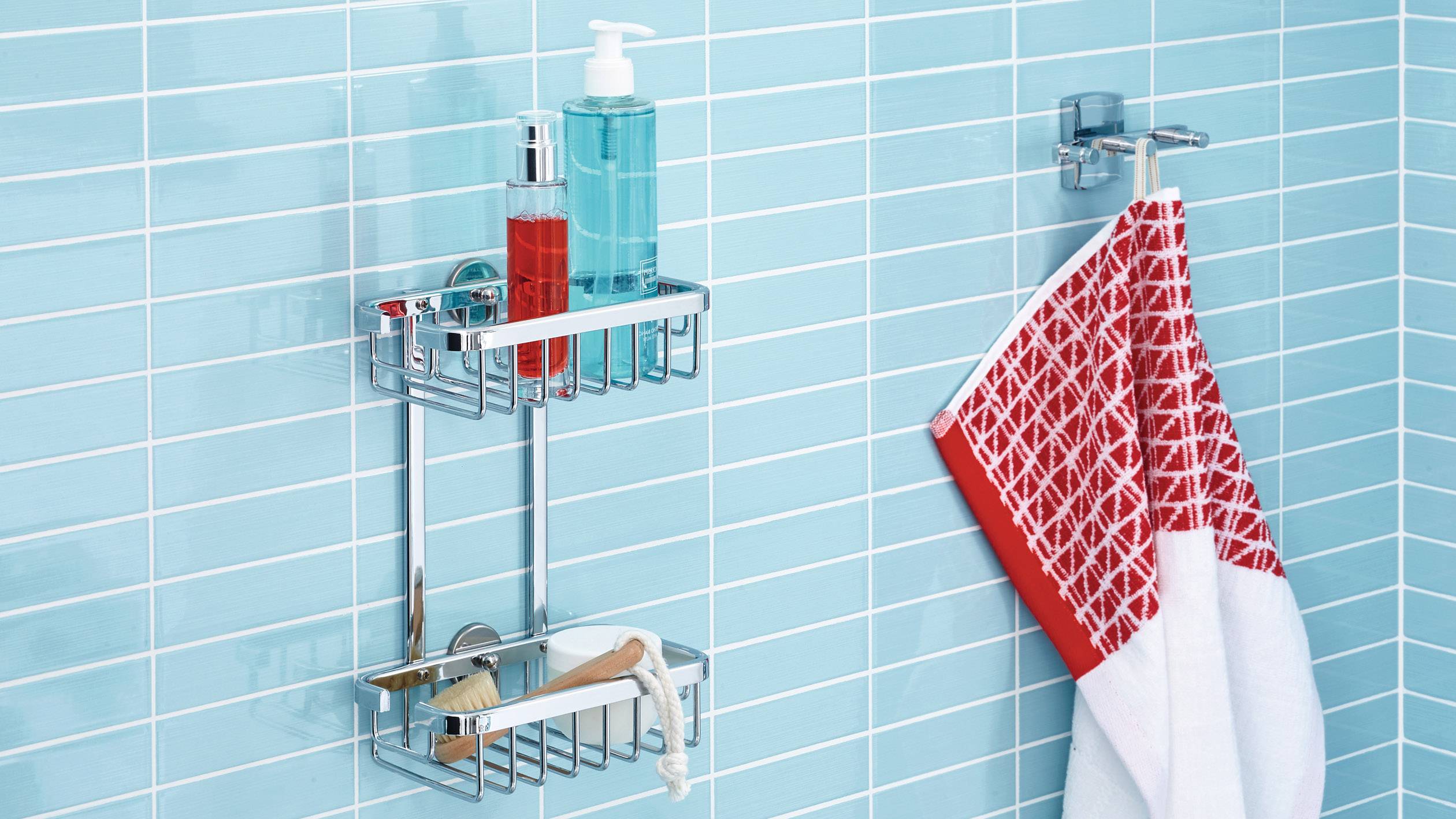 Kovový koupelnový regál s hygienickými potřebami, jako jsou dávkovače mýdla a kartáče, je připevněn na modře obložené stěně. Vedle něj visí červeno-bílý ručník.