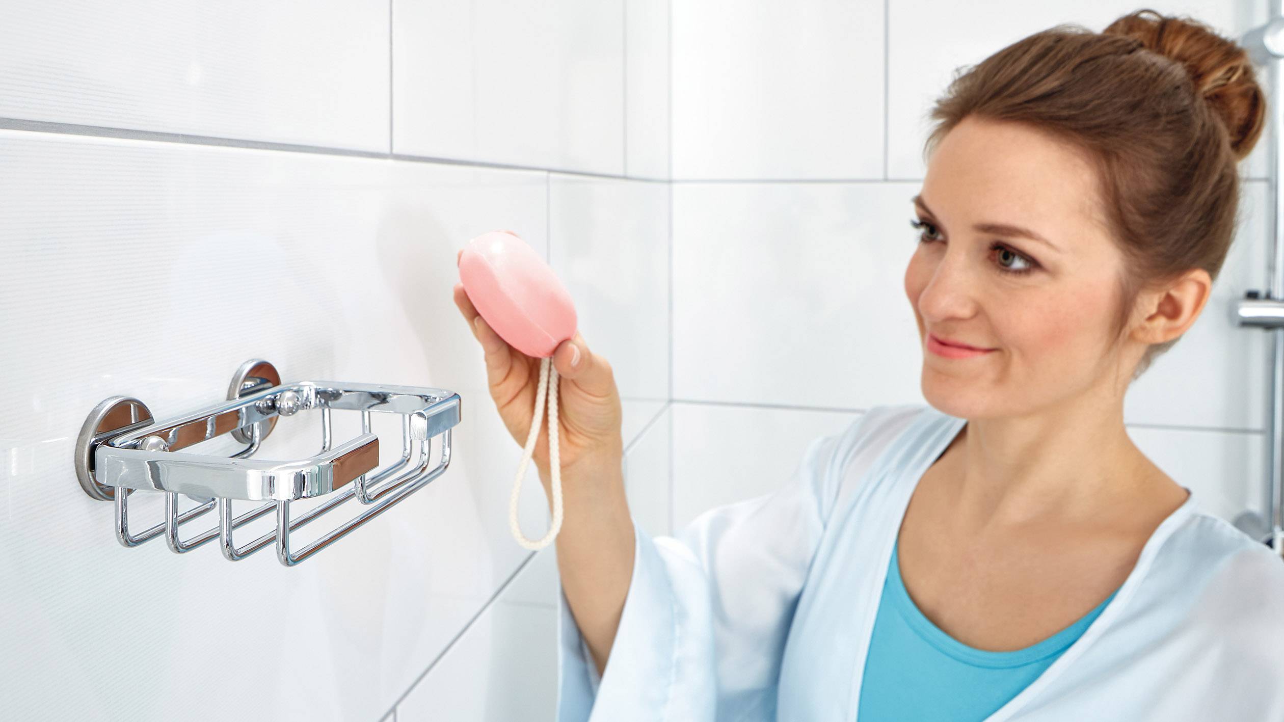 Žena v županu zavěšuje kus mýdla do držáku ve své koupelně, aby nastolila pořádek.