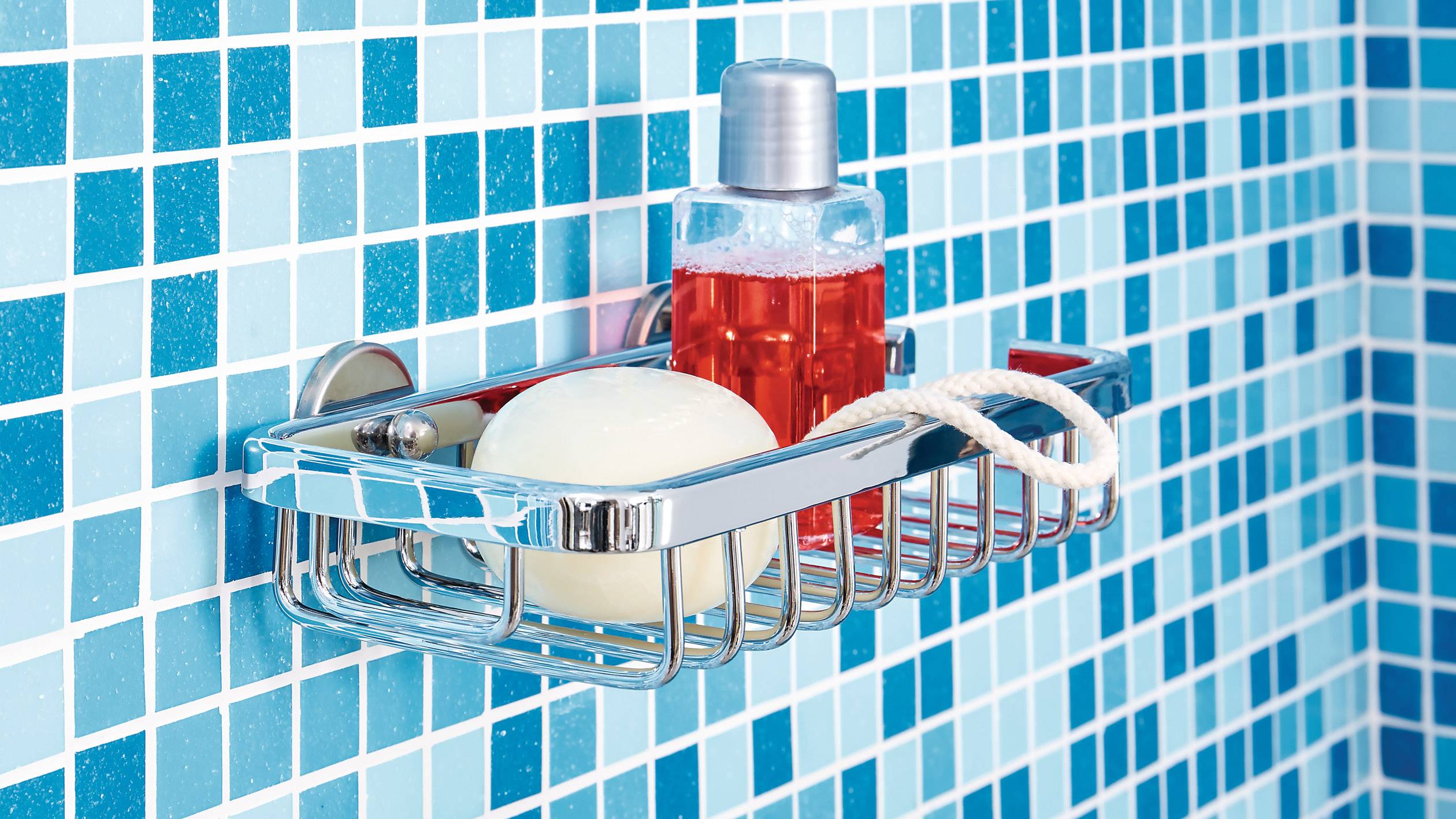 Sprchový koš na modře obložené stěně s kulatým mýdlem a červeným sprchových gelem.