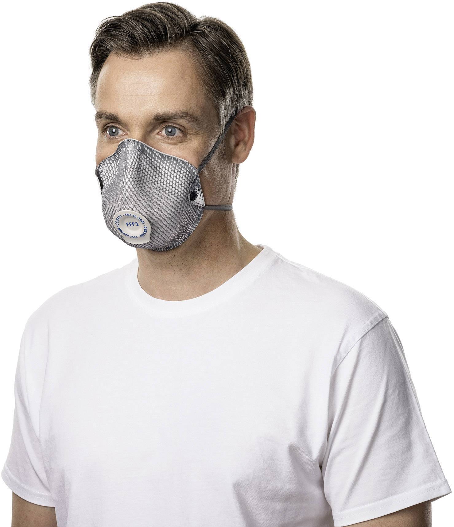 Muž nosí šedou respirační masku a bílé tričko. Dívá se dopředu.